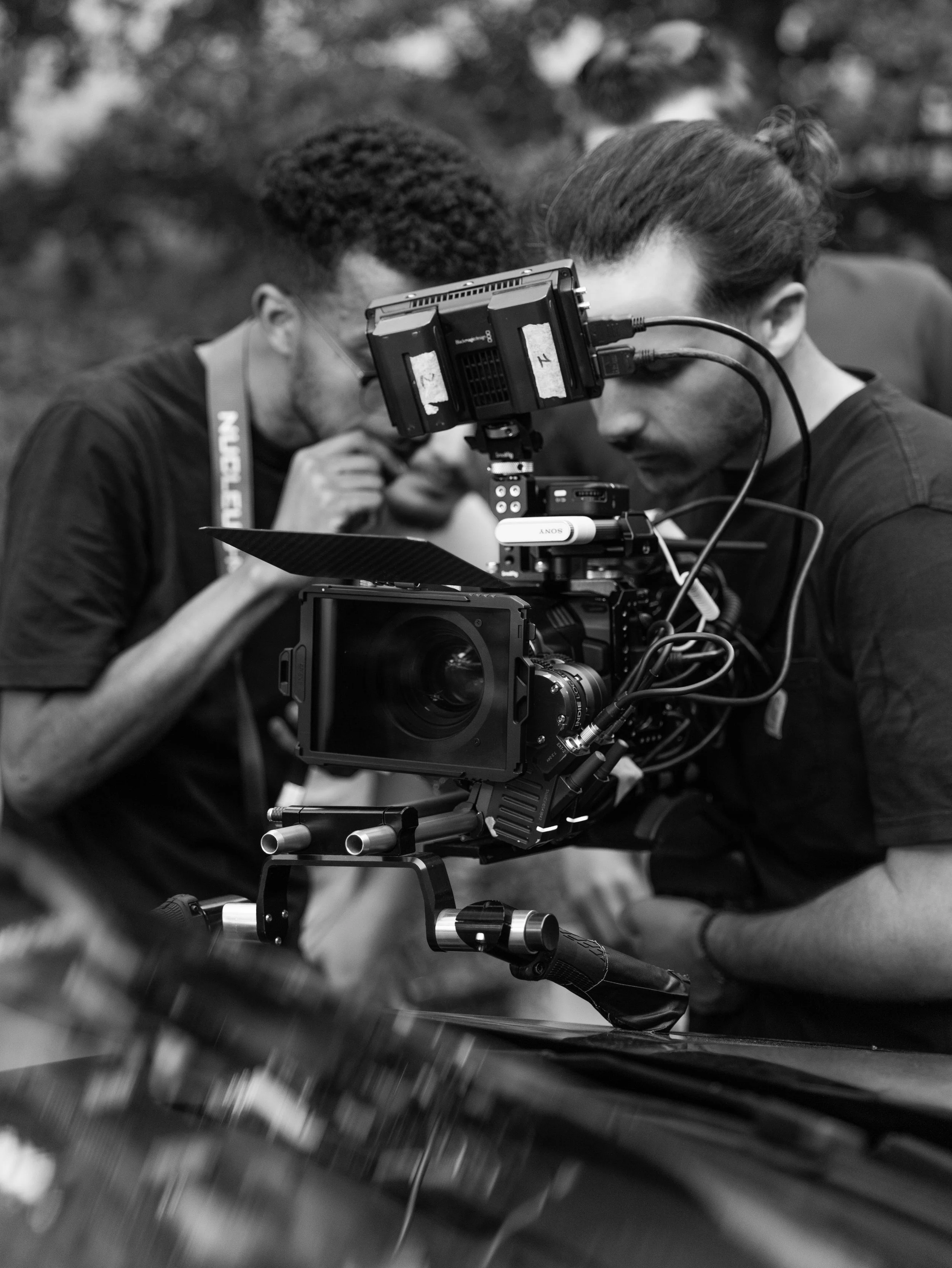 Deux personnes, équipées de matériel de tournage professionnel, examinent une caméra sur un plateau de tournage.