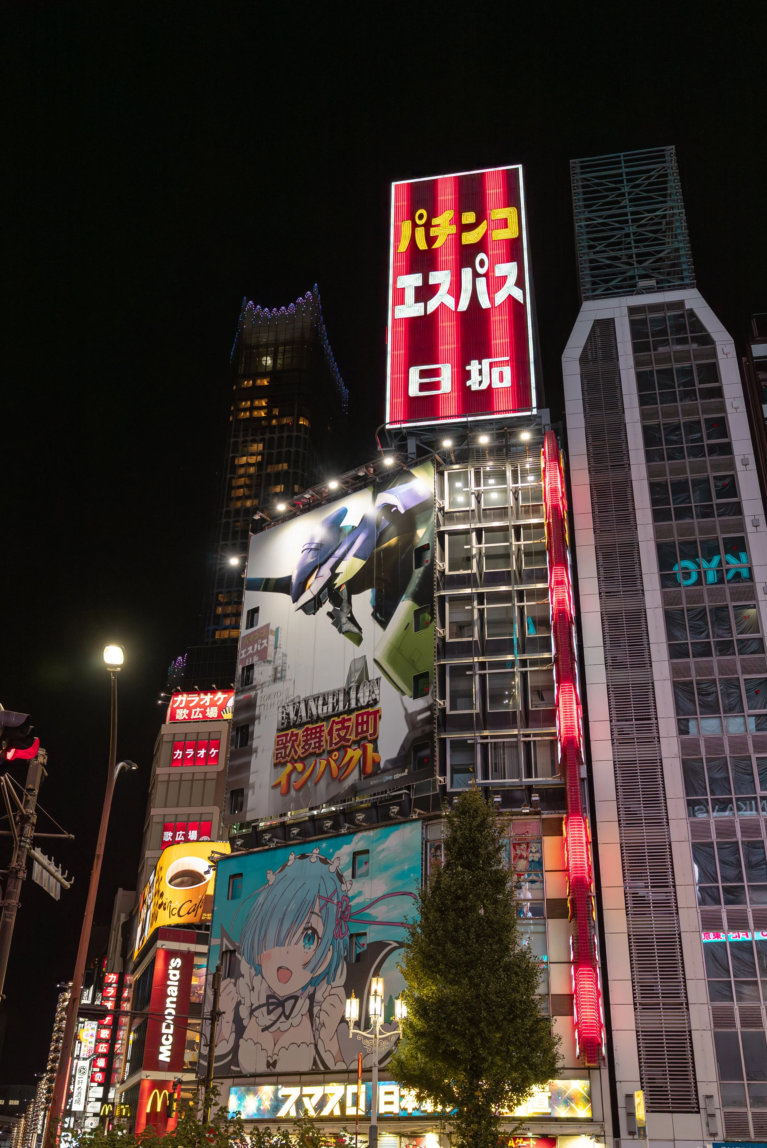 Édifice avec plusieurs écrans lumineux affichant des publicités colorées, dont une avec un avion et une anime, dans un quartier animé la nuit.