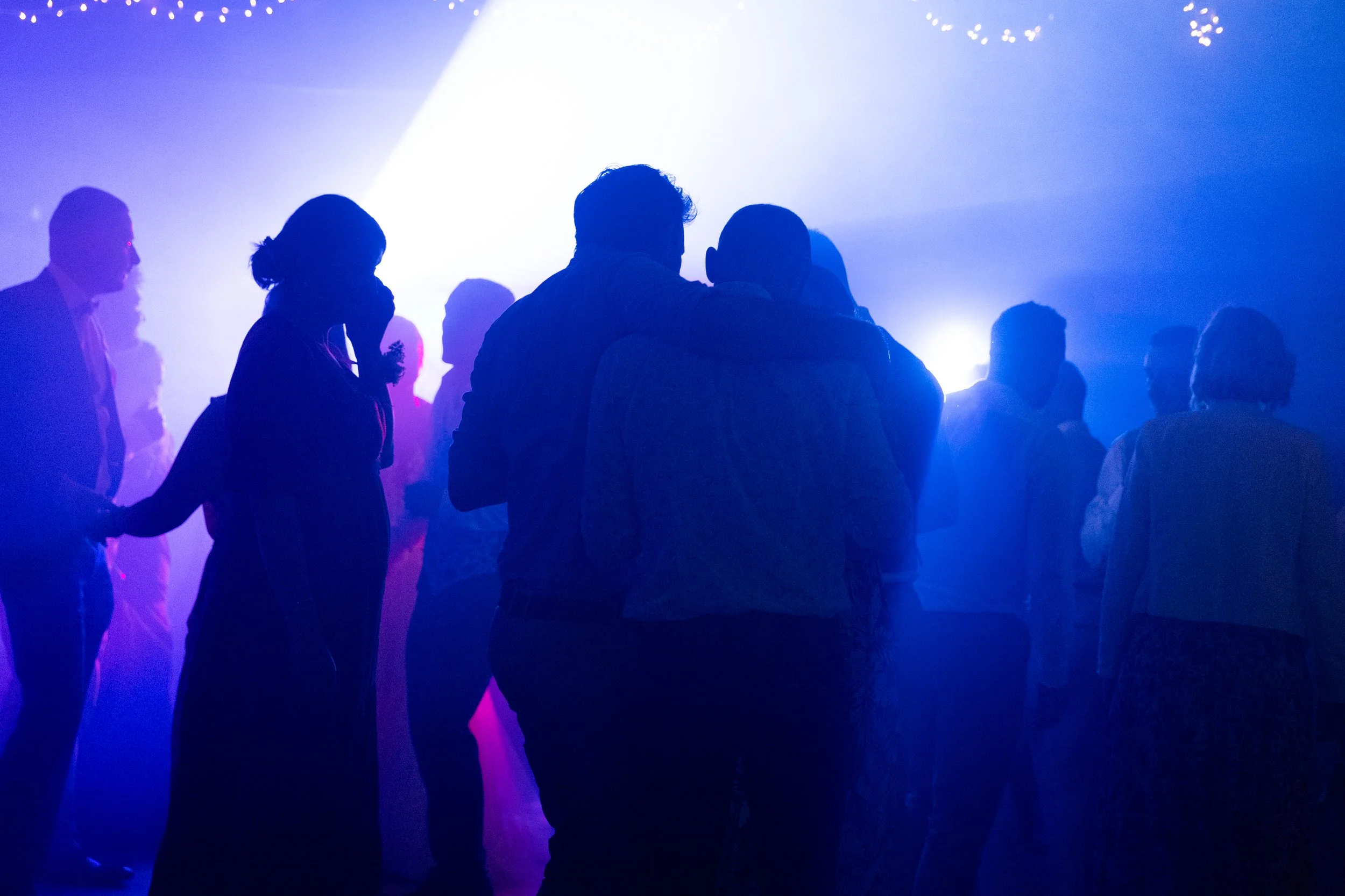 Groupe de personnes dans une salle sombre avec éclairage bleu, certains dansant ou socialisant.