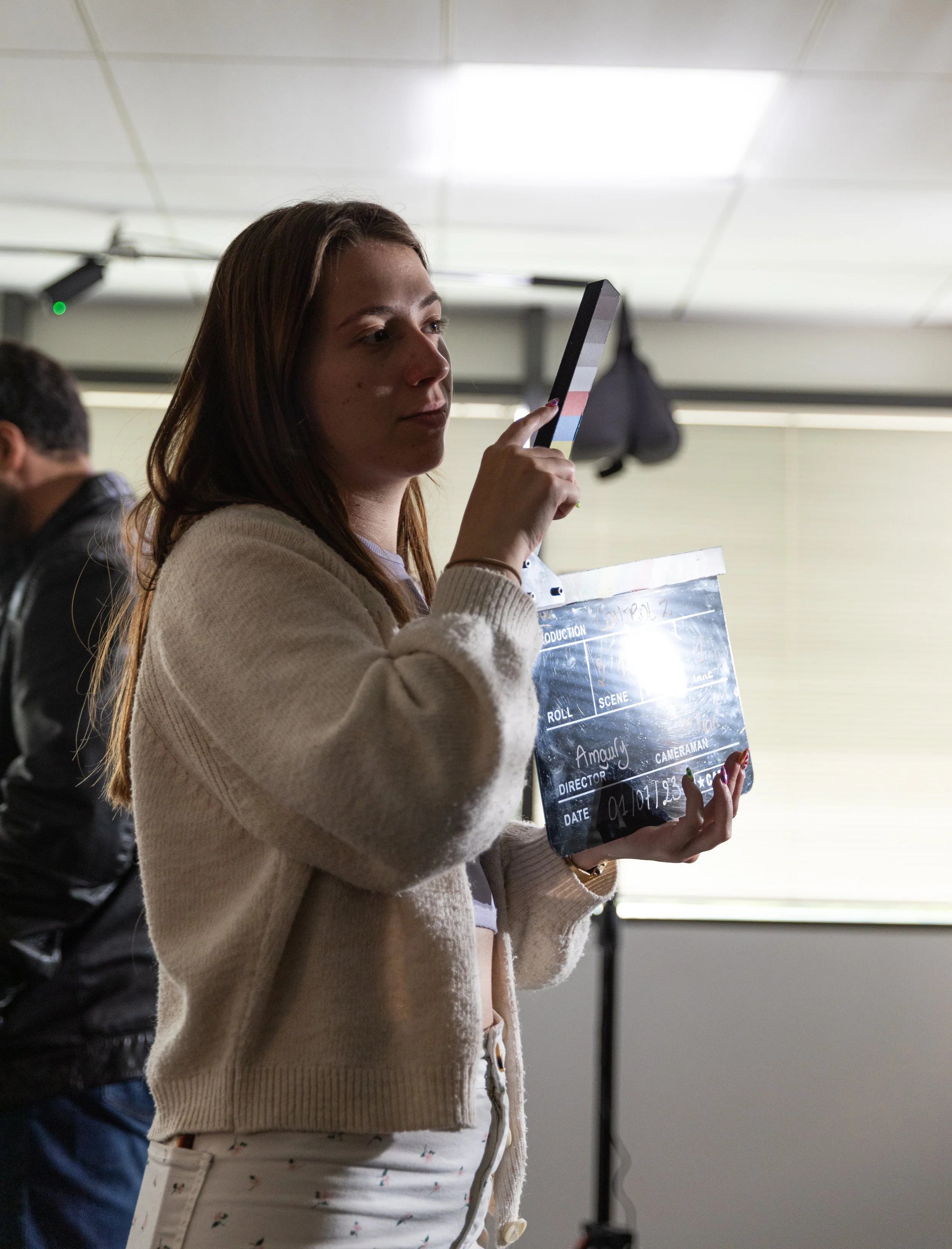 Une femme tient une planche de clap de film en regardant un smartphone, dans un environnement intérieur.