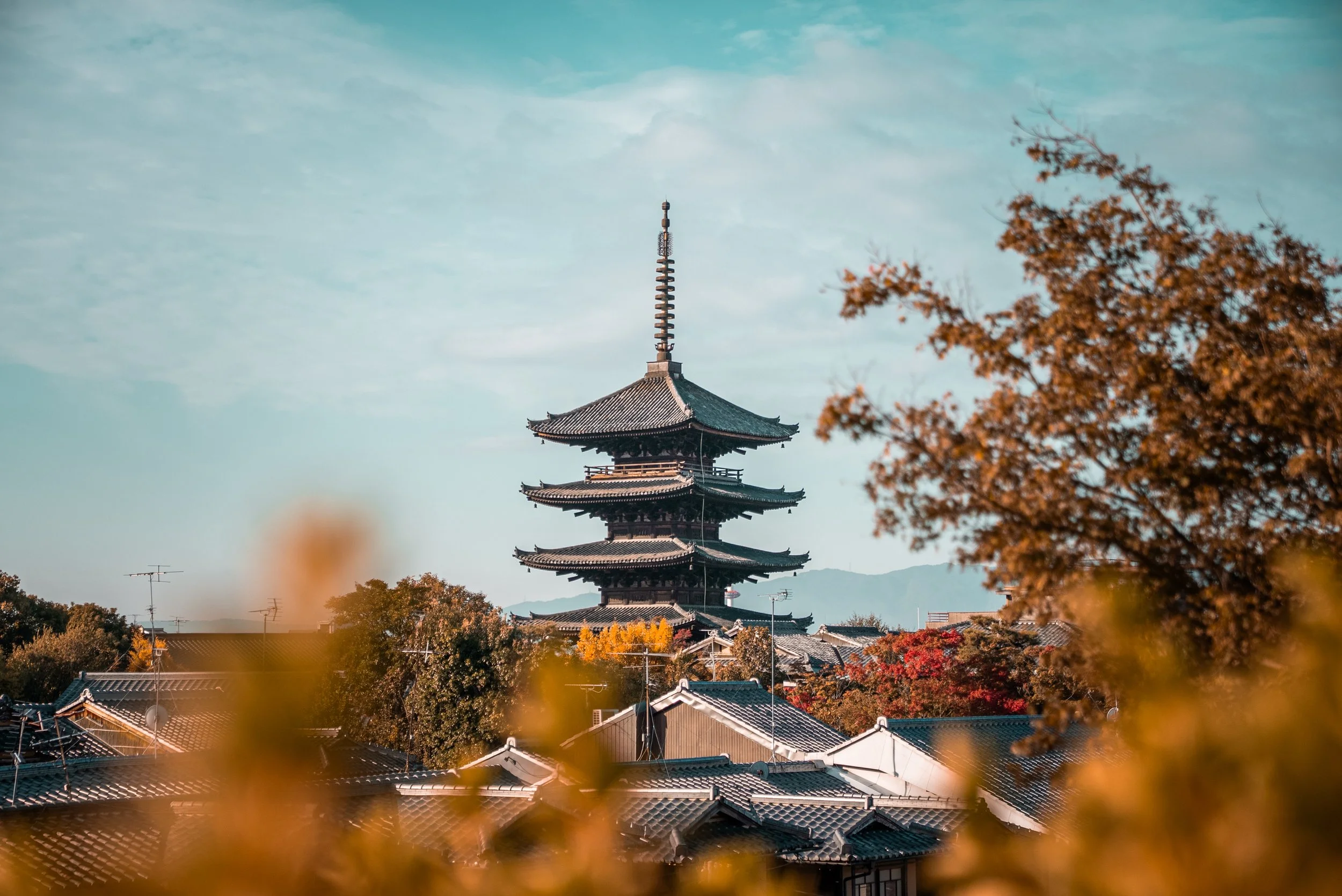 Une pagode traditionnelle japonaise entourée d'arbres aux couleurs automnales, avec un ciel légèrement nuageux en arrière-plan.