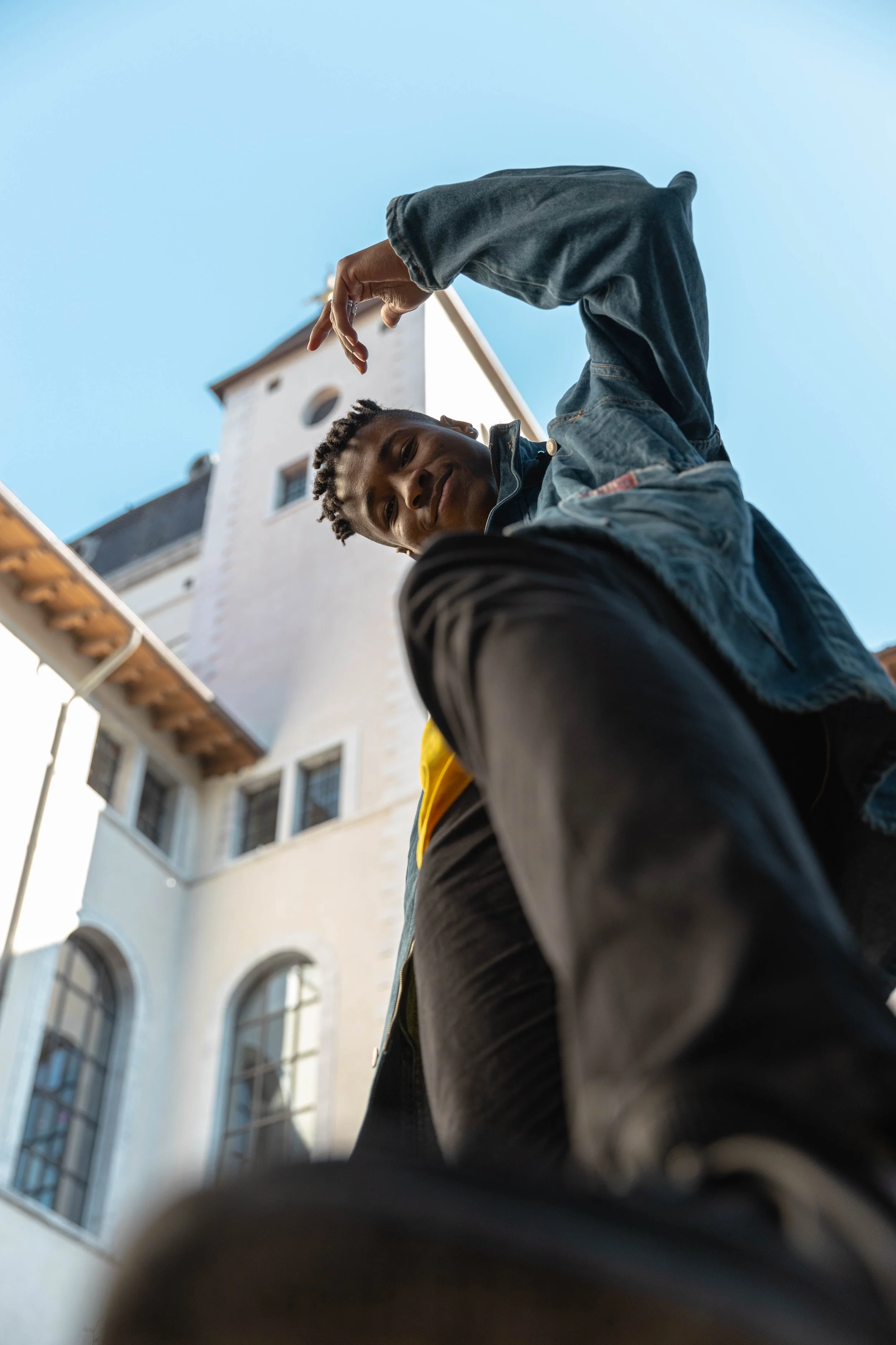 Jeune homme regardant en bas, pris d'un angle en contre-plongée à côté d'un bâtiment historique avec une tour, ciel clair.