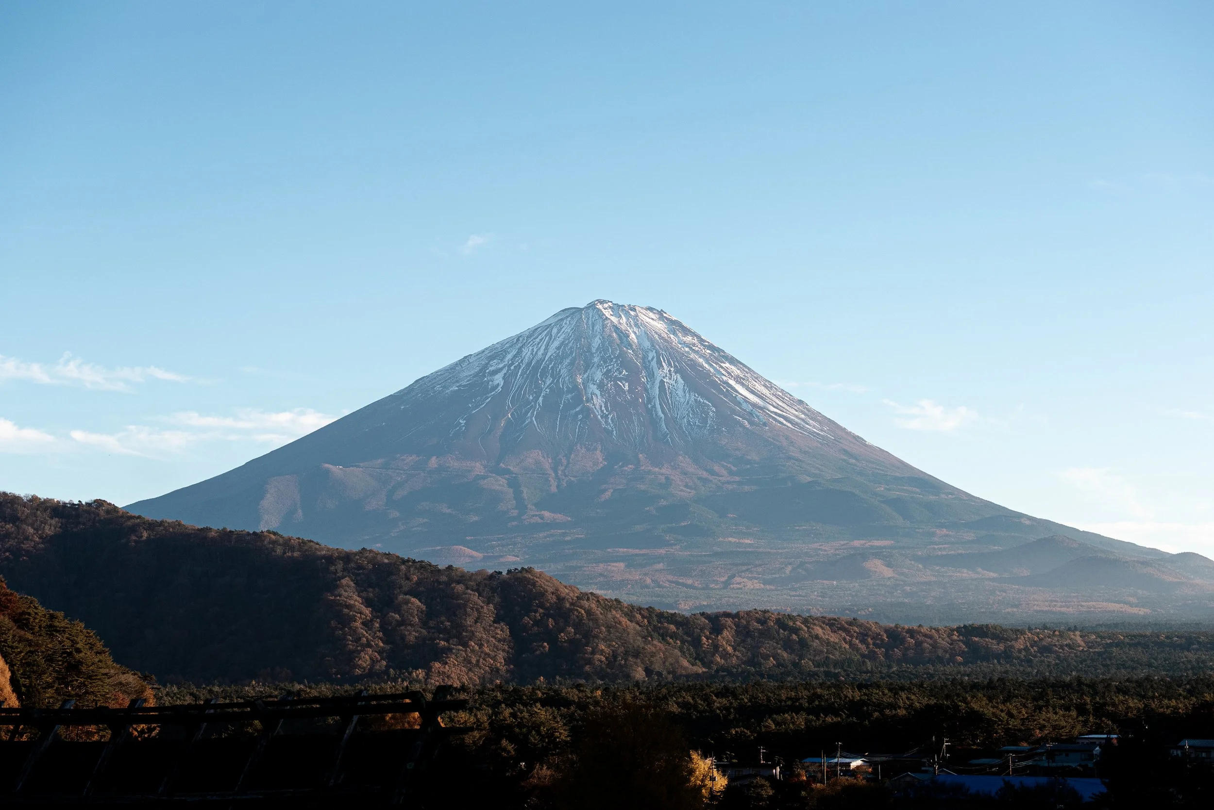 Mont Fuji avec neige au sommet, entouré de montagnes et un ciel clair.