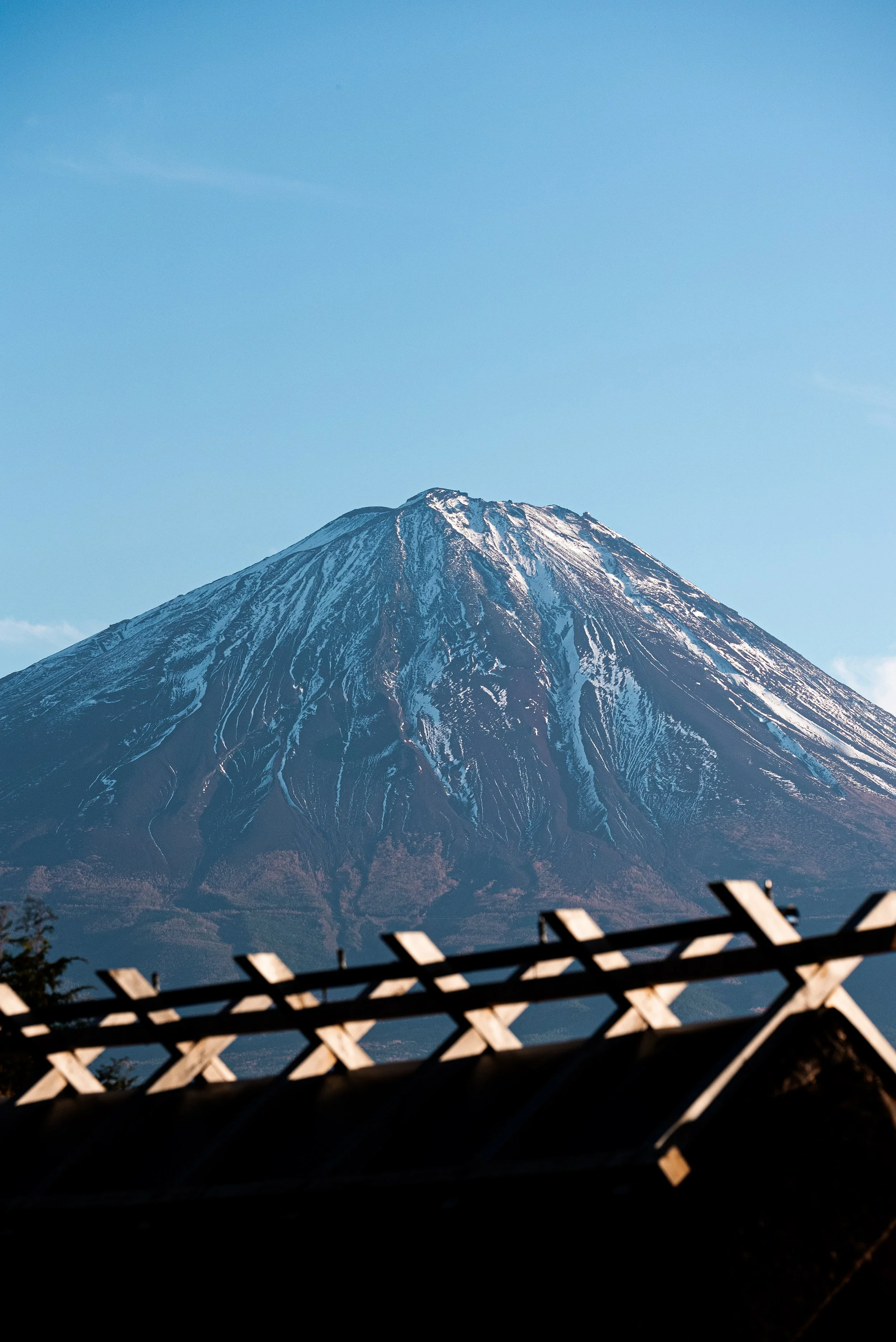 Vue du mont Fuji avec un ciel bleu clair et une structure en bois au premier plan.