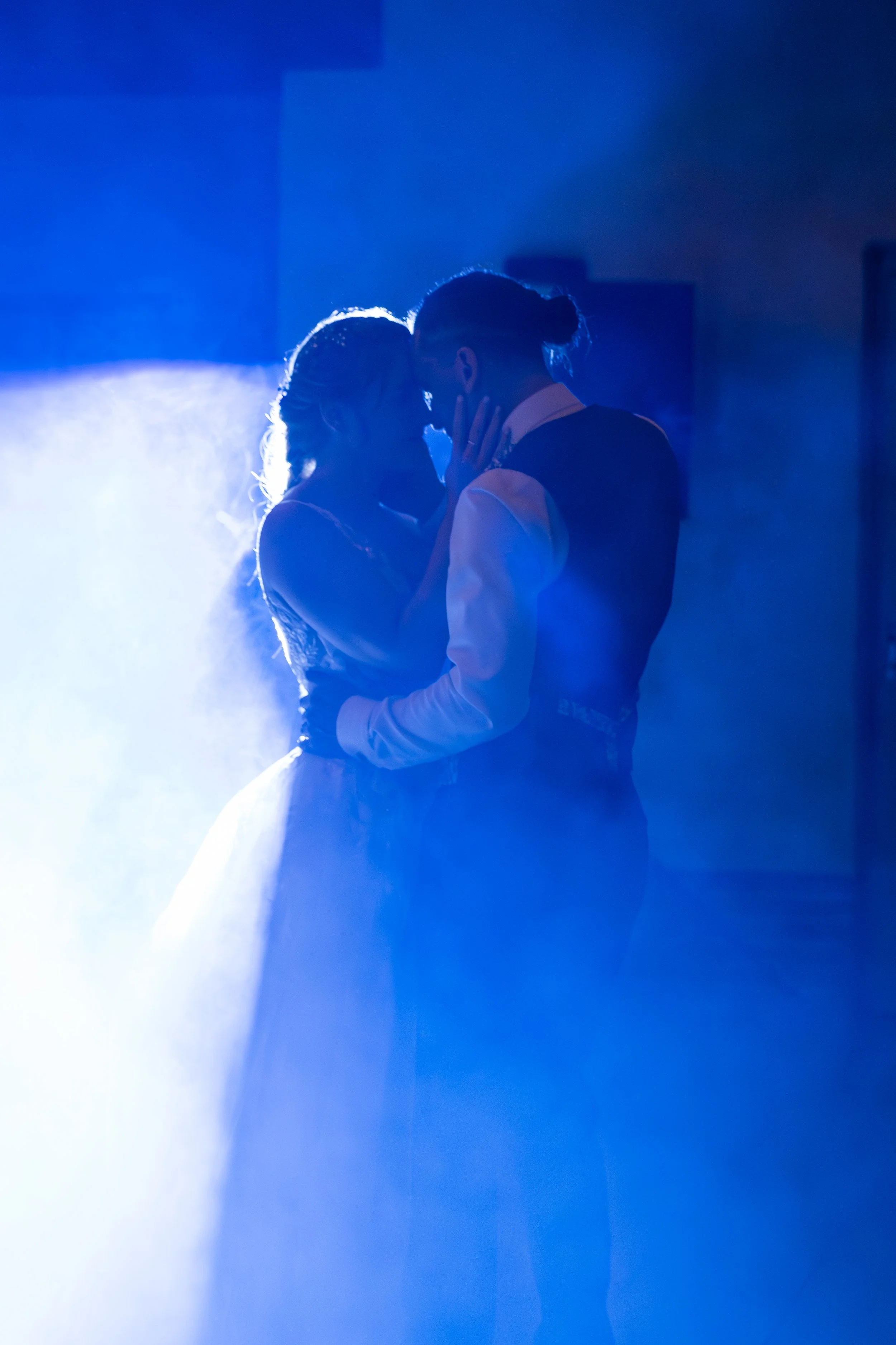 Deux personnes dansent en se regardant, entourées de brume, éclairées par une lumière bleue dans une pièce sombre.
