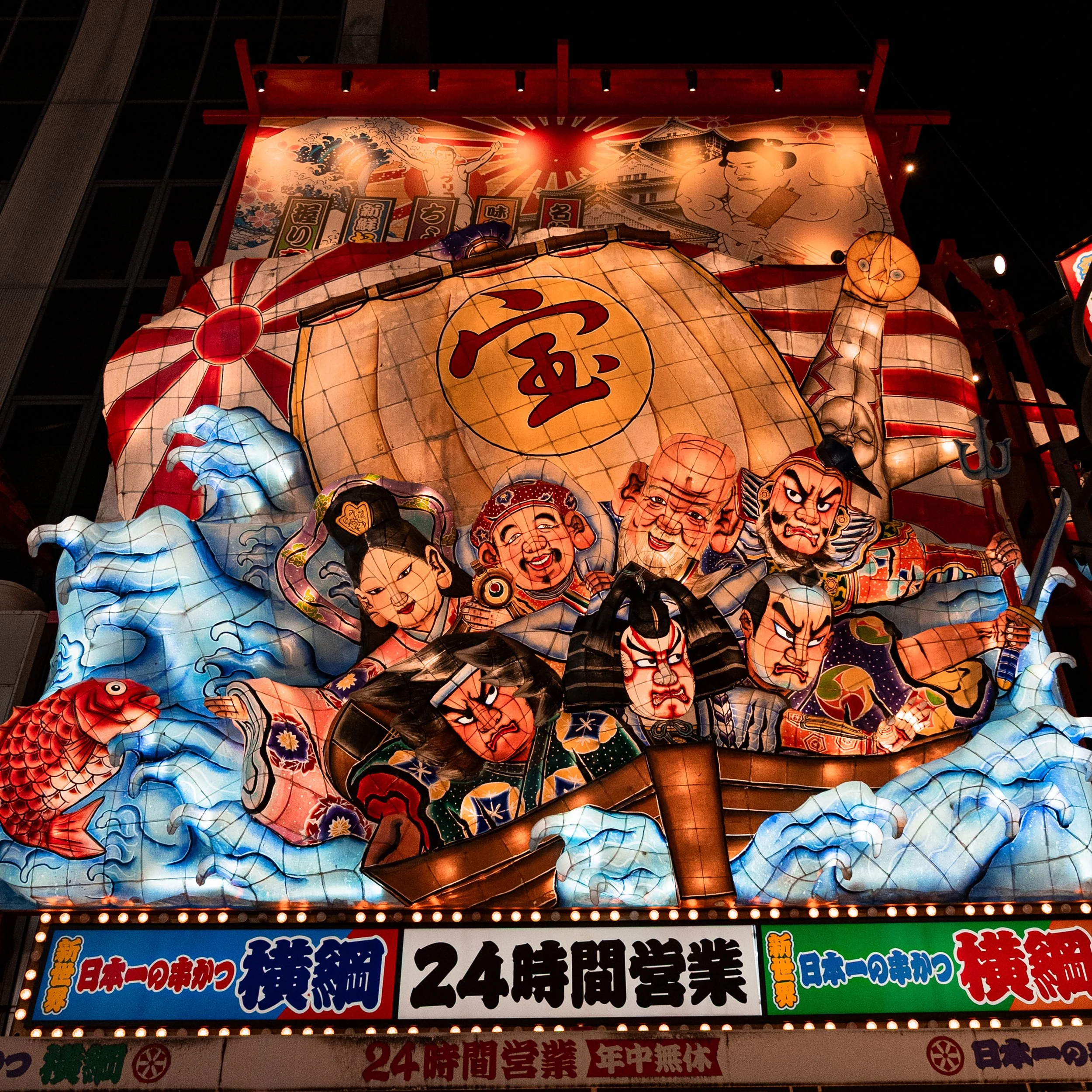 Une enseigne lumineuse traditionnelle japonaise représentant des personnages en papier lanternes, dont des samouraïs, un pêcheur et une femme, entourés de vagues et un poisson rouge, avec des panneaux indiquant une ouverture 24 heures.