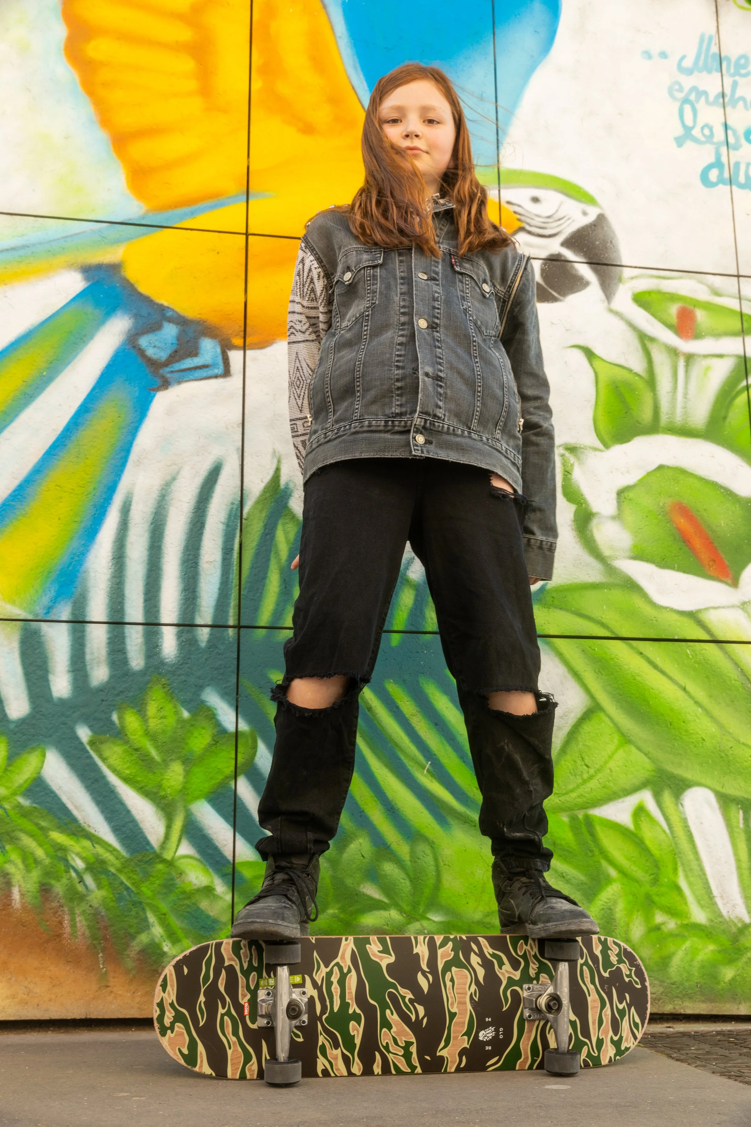 Jeune fille debout sur un skateboard avec un mur de graffiti en arrière-plan.