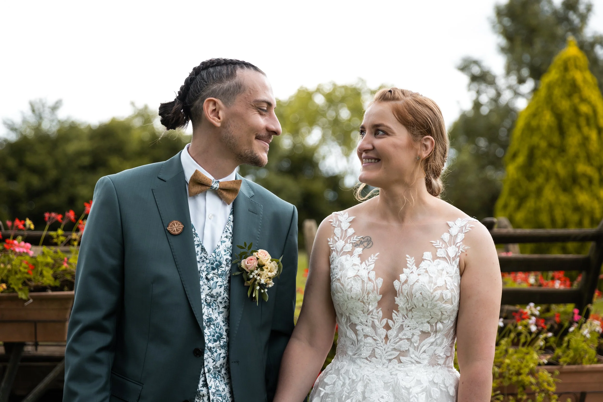 Un couple de mariés regarde l'un l'autre avec le sourire lors de leur mariage en extérieur, entouré de fleurs et d'arbres.