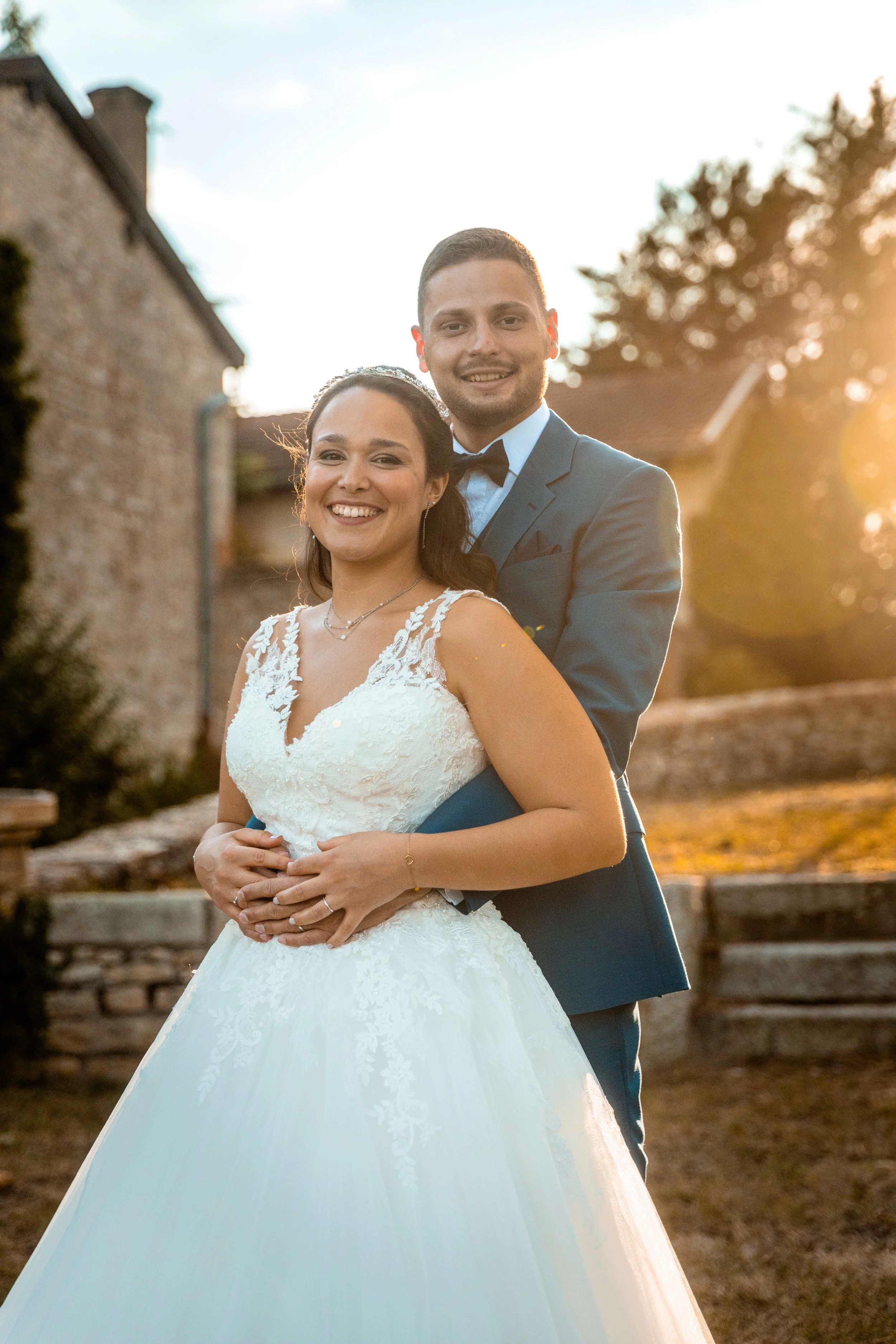 Un couple en tenue de mariage posant à l'extérieur avec un coucher de soleil en arrière-plan.