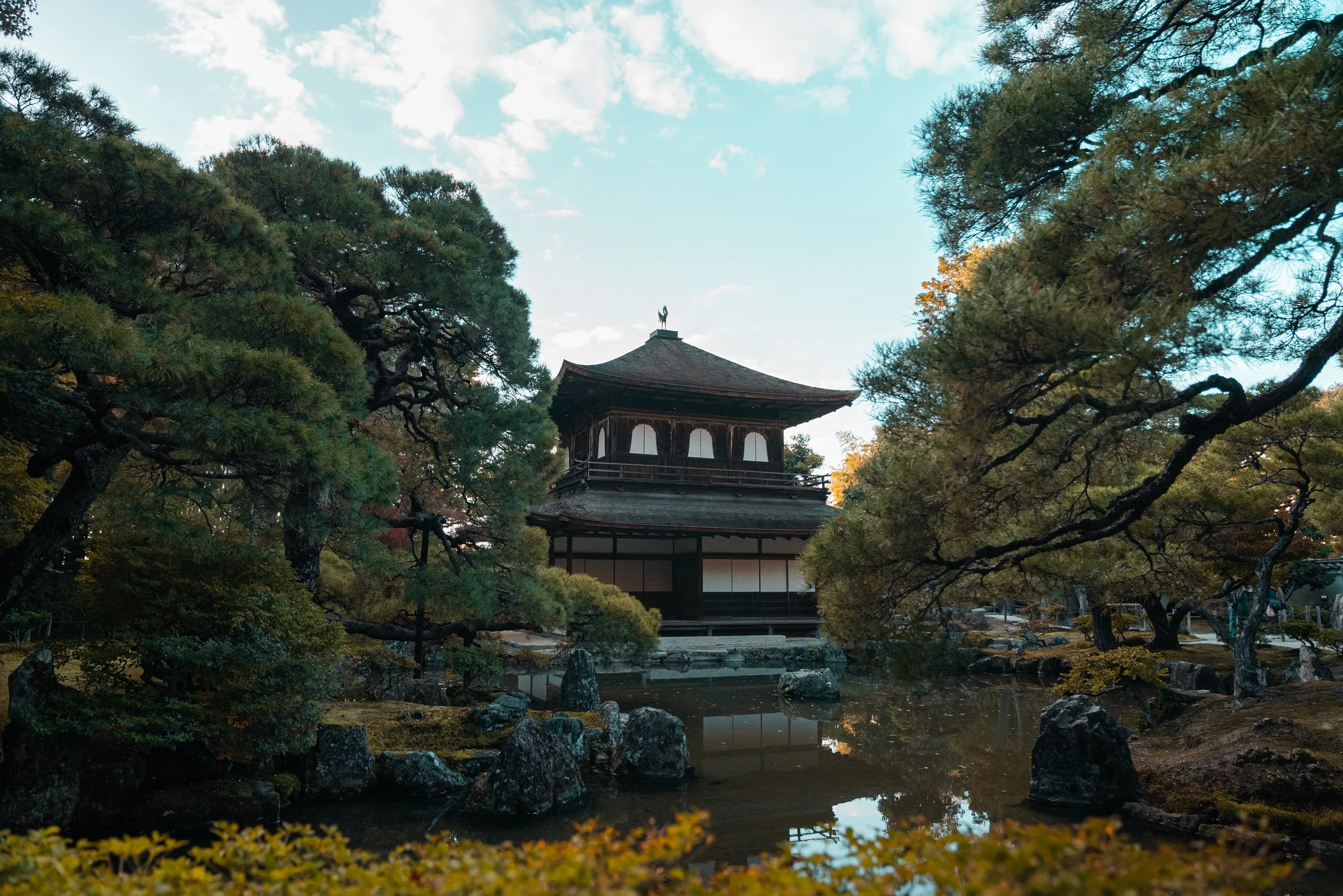 Une pagode traditionnelle japonaise entourée d'arbres dans un jardin avec un étang au premier plan.