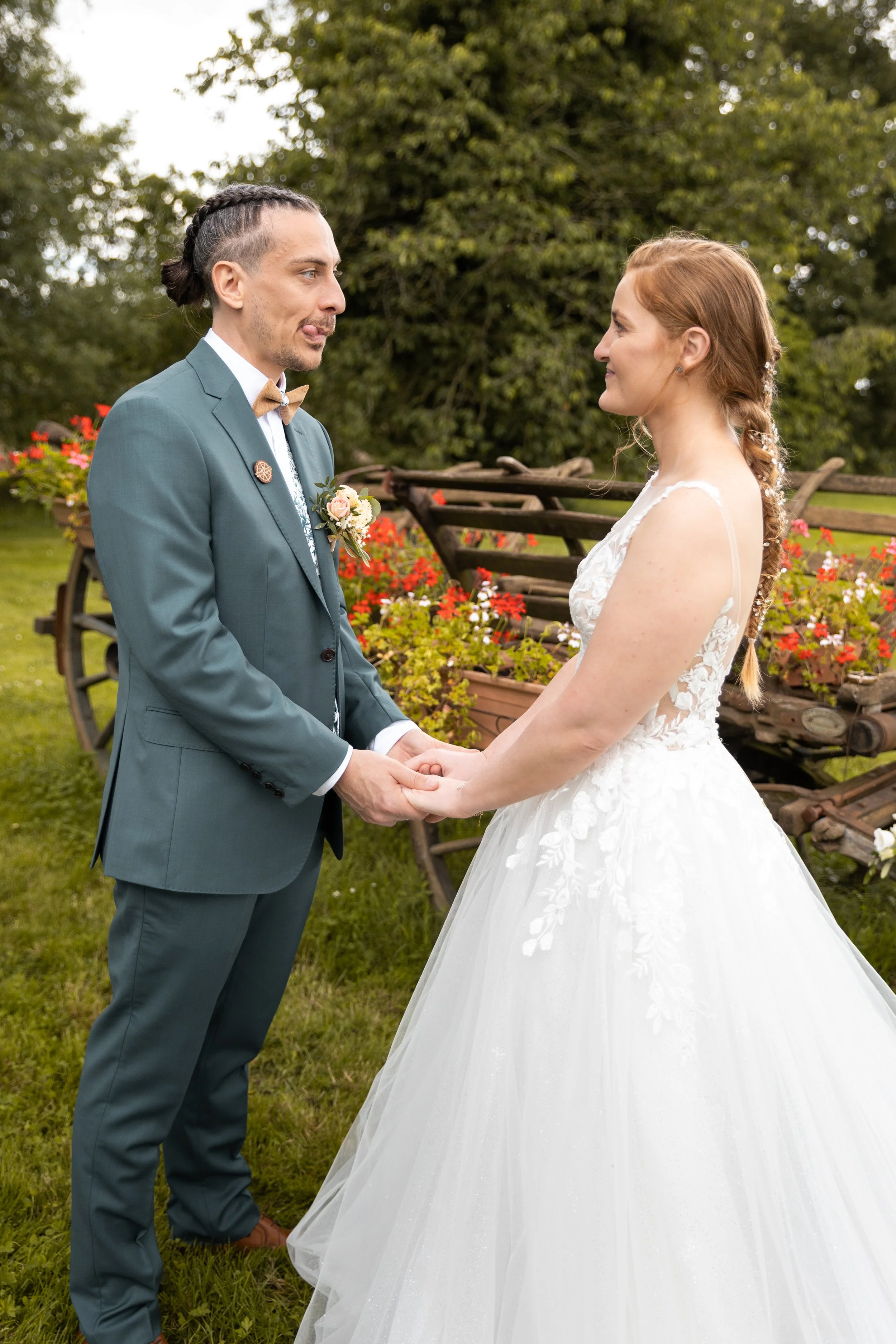Un couple en mariage échangeant leurs vœux en plein air avec un décor de fleurs et de vieux chariots en arrière-plan.