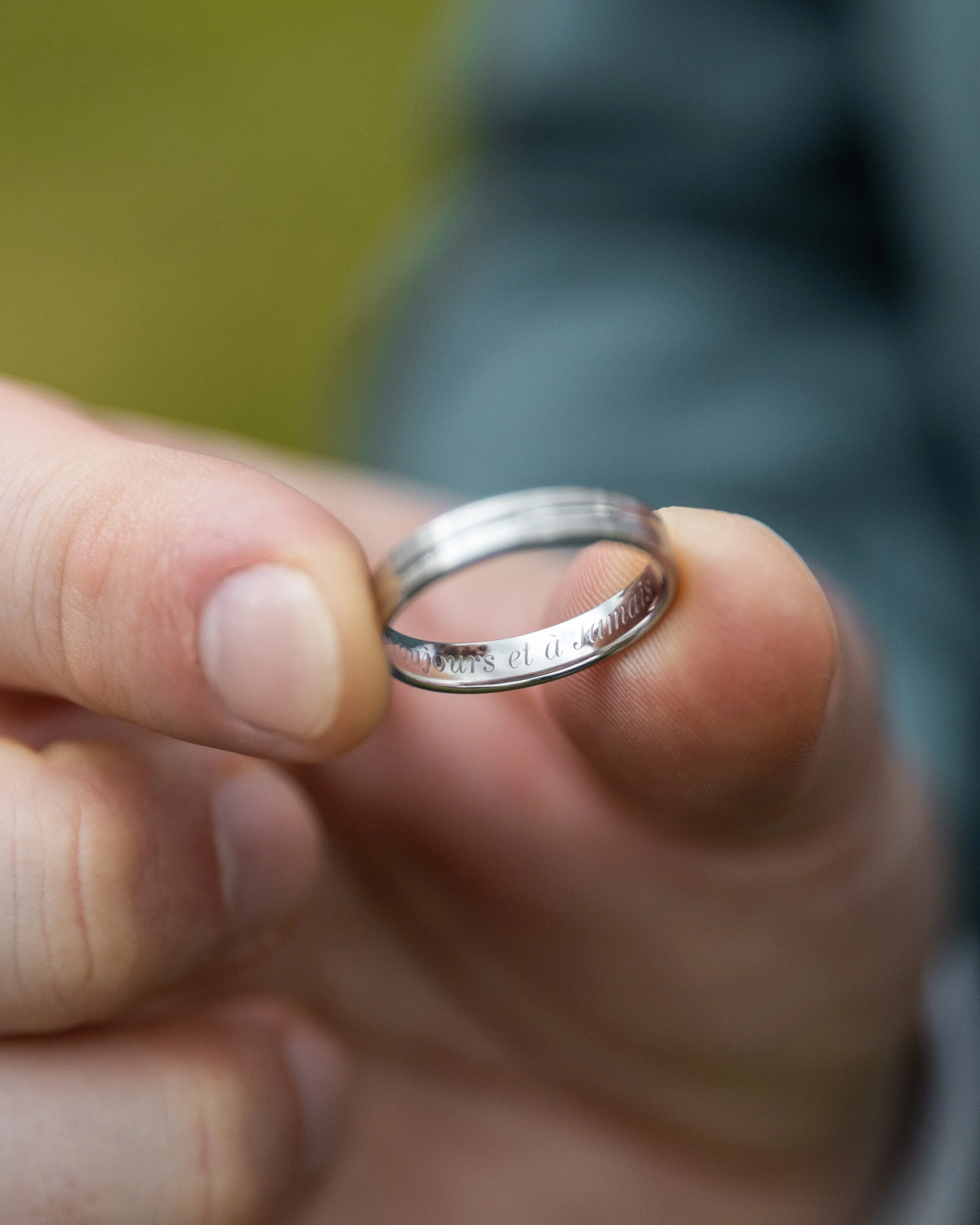 Une main tient une alliance en métal gravée, avec une inscription partielle visible en français.