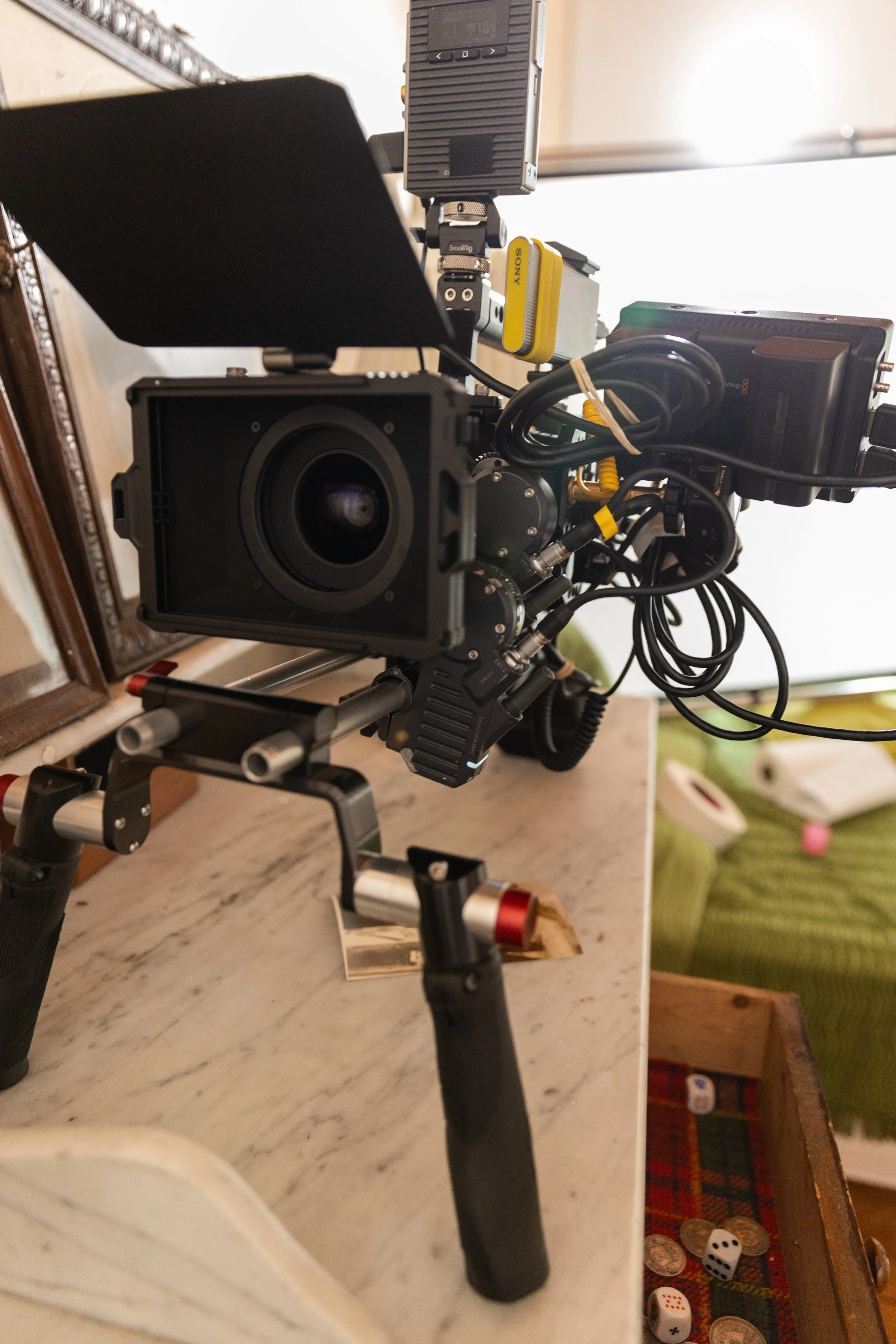 Caméra de haute technologie, équipée de divers câbles et accessoires, positionnée sur une surface en marbre, avec un miroir ancien et des dés de jeu à proximité