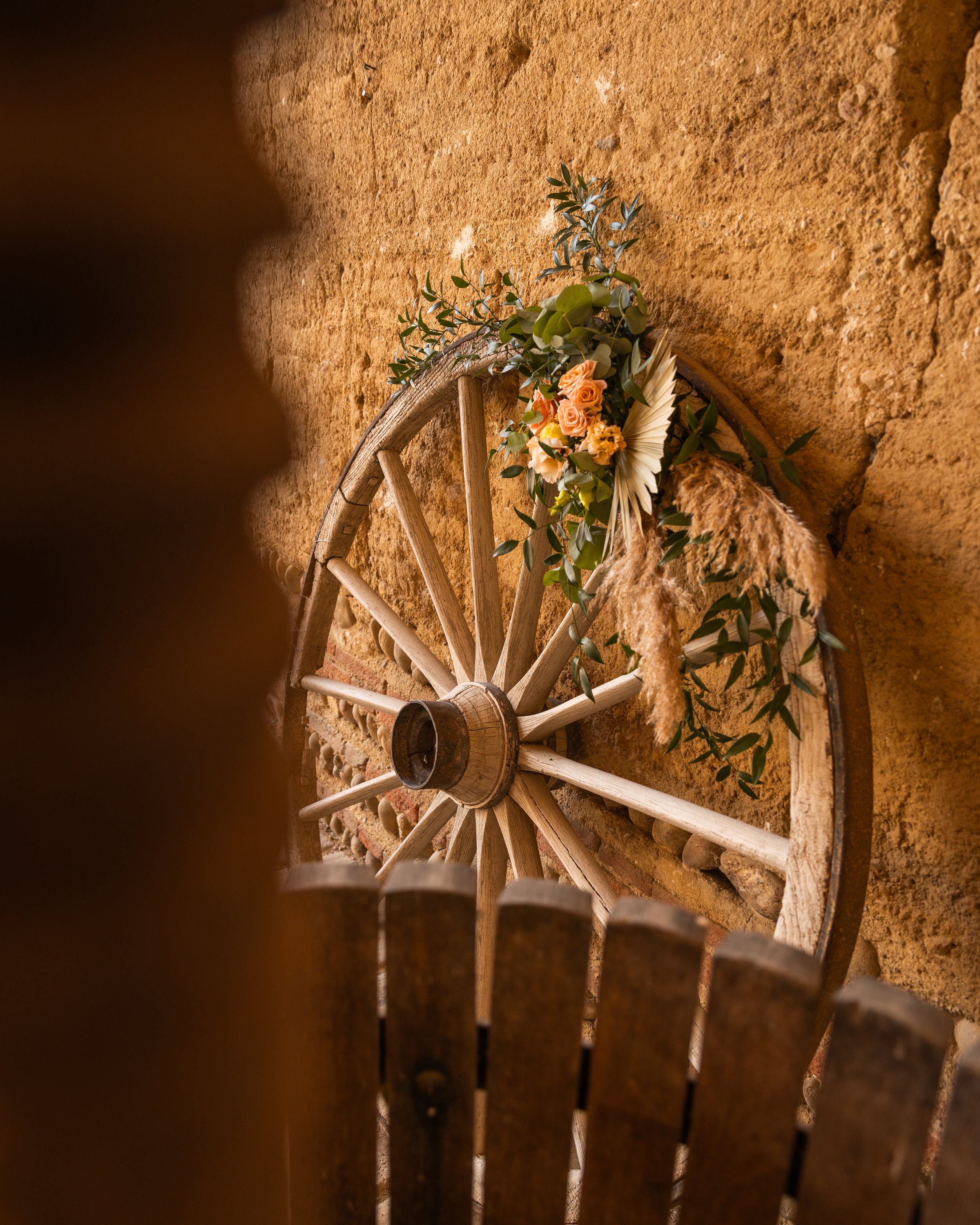 Une roue en bois décorée de fleurs dans un cadre rustique contre un mur en terre cuite.