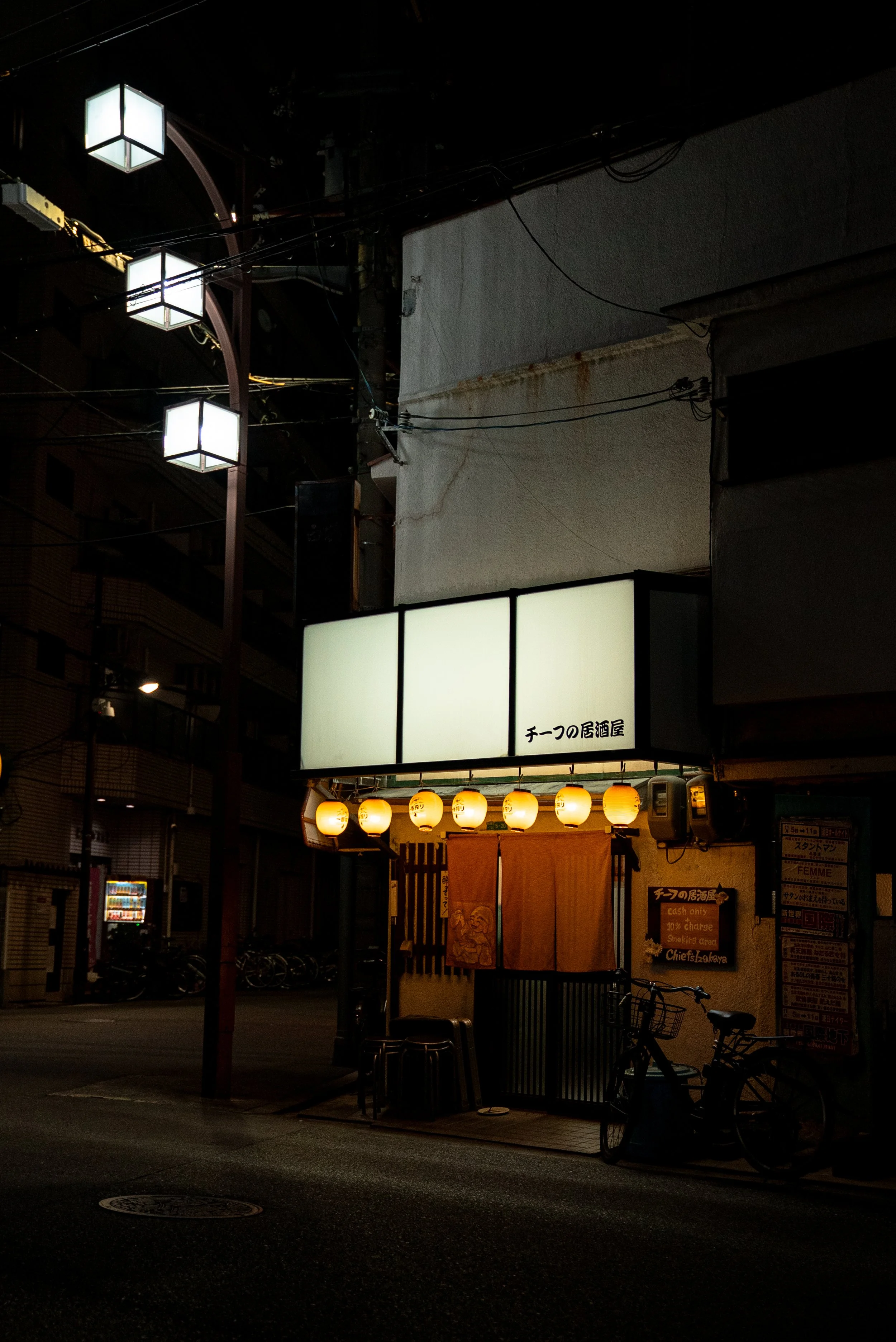 Façade d'un restaurant japonais avec des lanternes en papier et un panneau lumineux, la nuit.