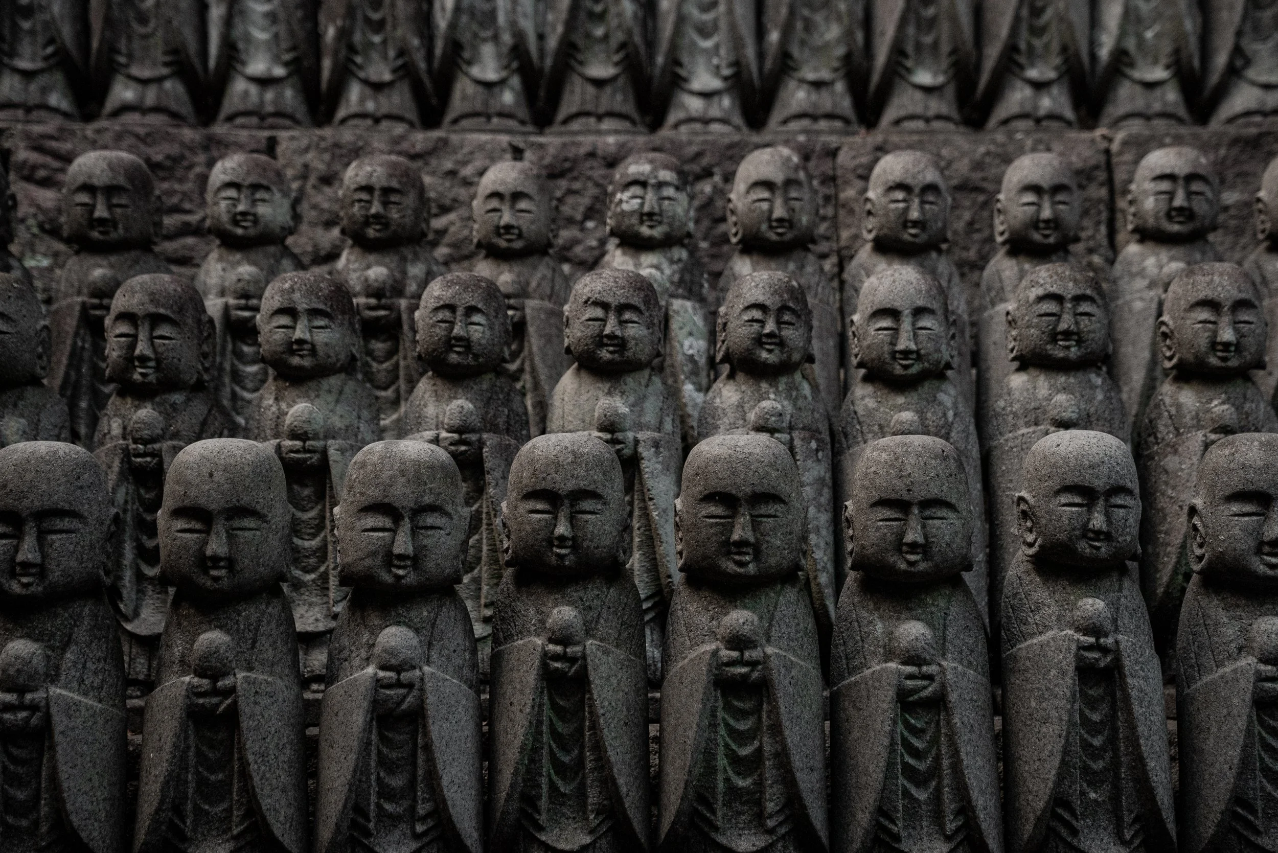 Statues en pierre représentant des figures bouddhistes alignées en rangées devant un mur en pierre.