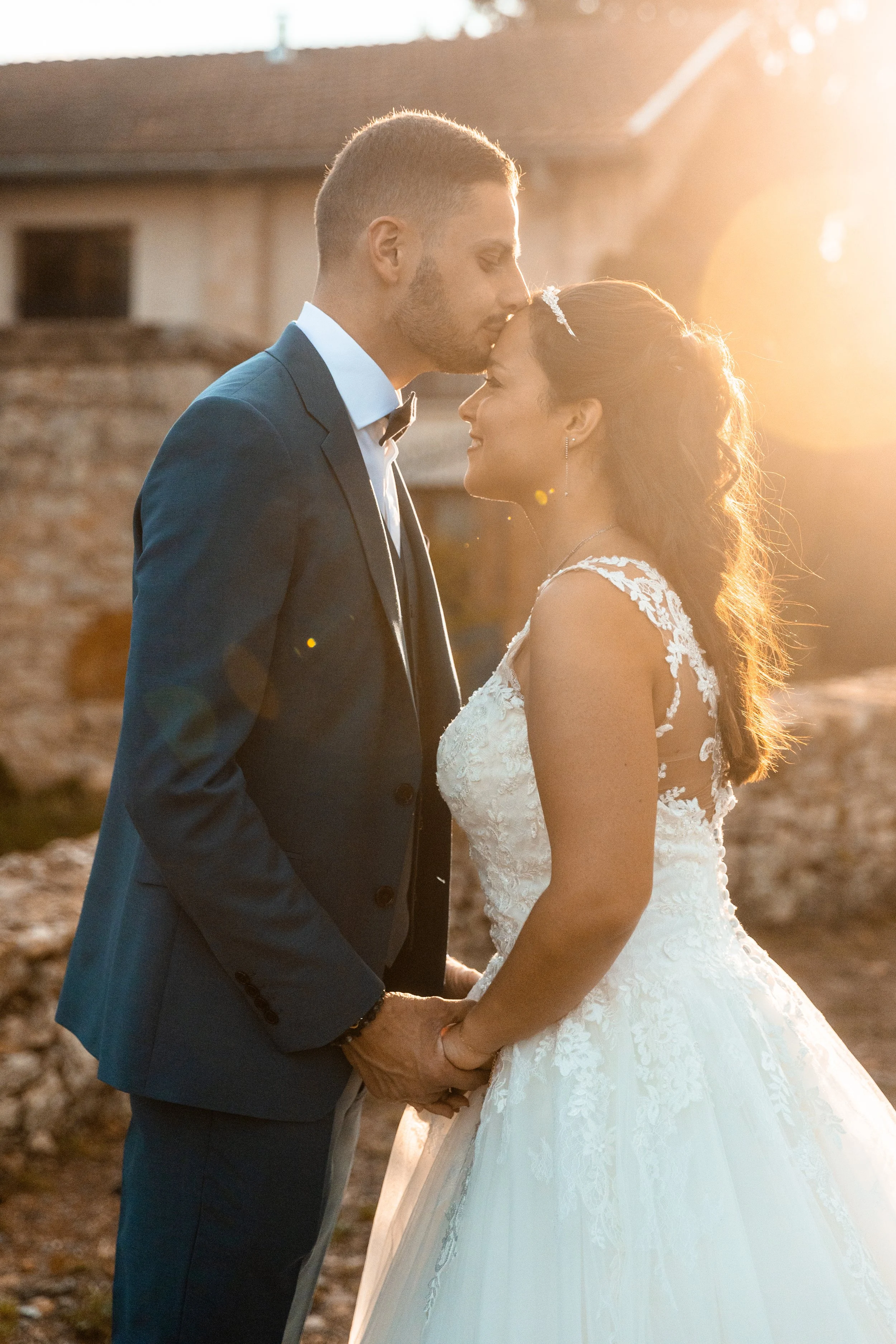 Un couple marié en tenue de mariage, tenant la main, dans un endroit extérieur au coucher du soleil.