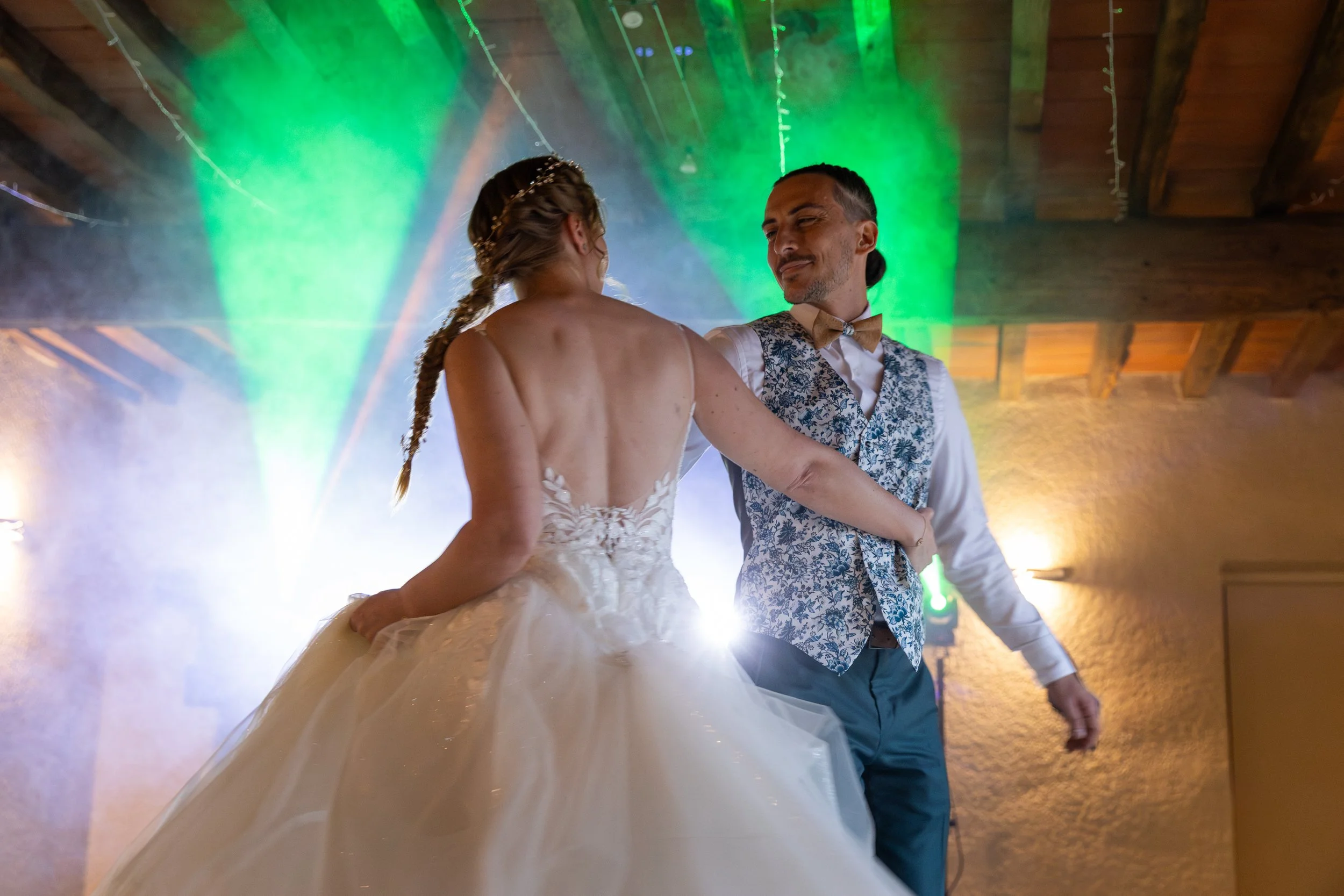 Un couple danse lors d'une réception de mariage, avec des lumières vertes et un décor chaleureux en arrière-plan.