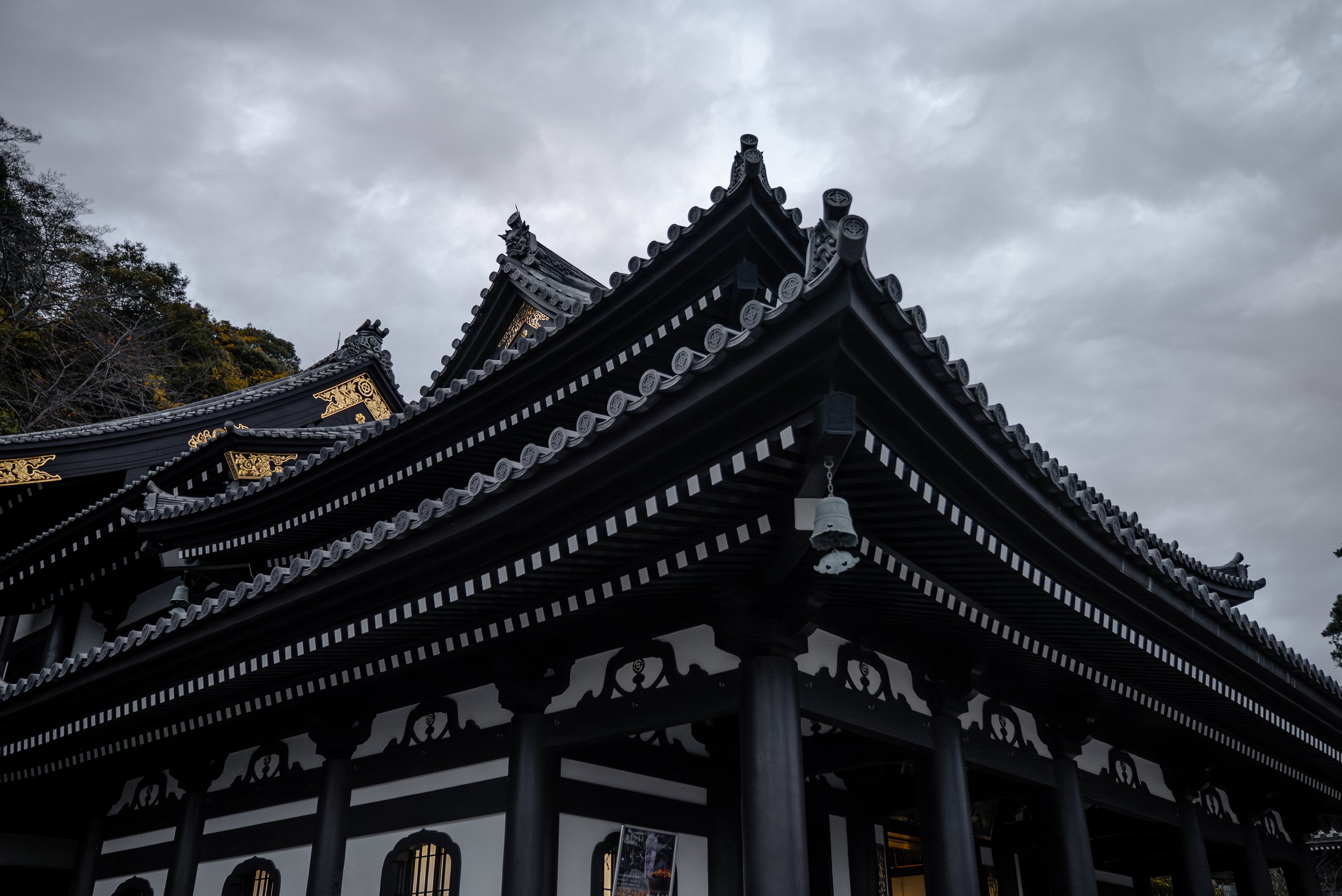 Vue d'un bâtiment traditionnel japonais avec des toits en tuiles noires ornementés, sous un ciel nuageux.