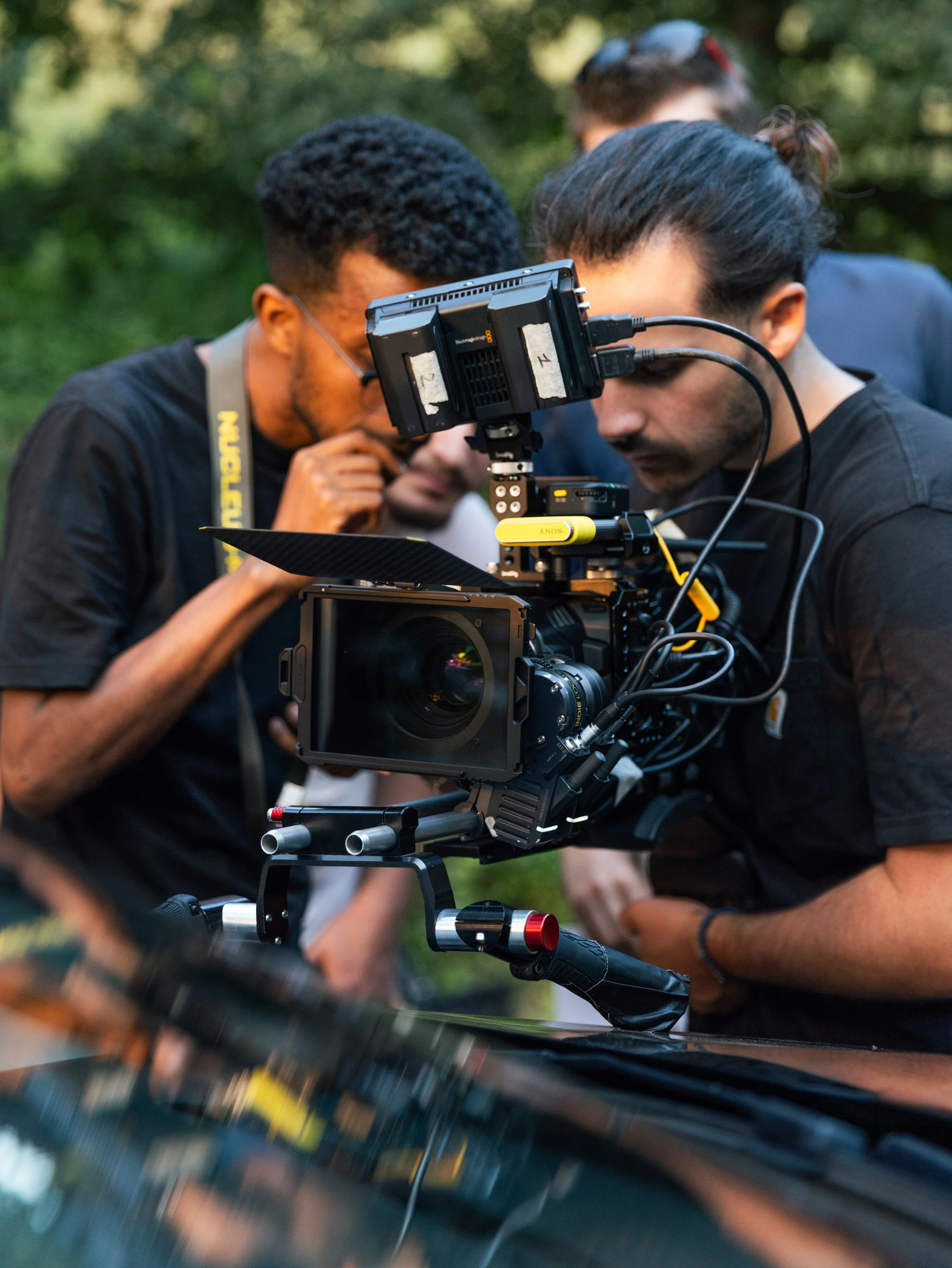 Une équipe de cinéastes ou de vidéastes en train de régler une caméra professionnelle lors d'un tournage en extérieur, dans un environnement verdoyant.