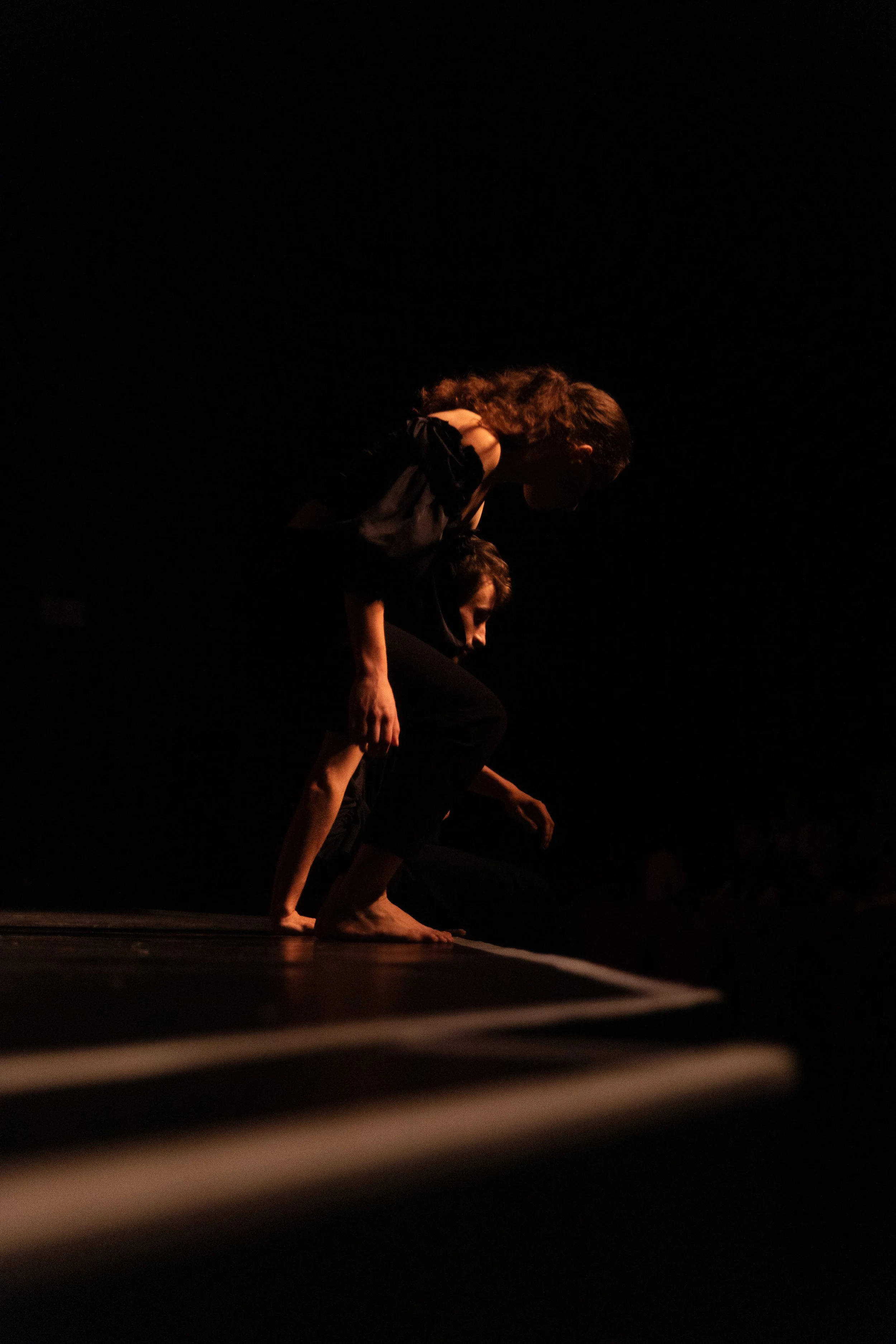 Deux femmes pratiquant une danse ou une acrobatie au sol, dans un environnement sombre avec une lumière tamisée