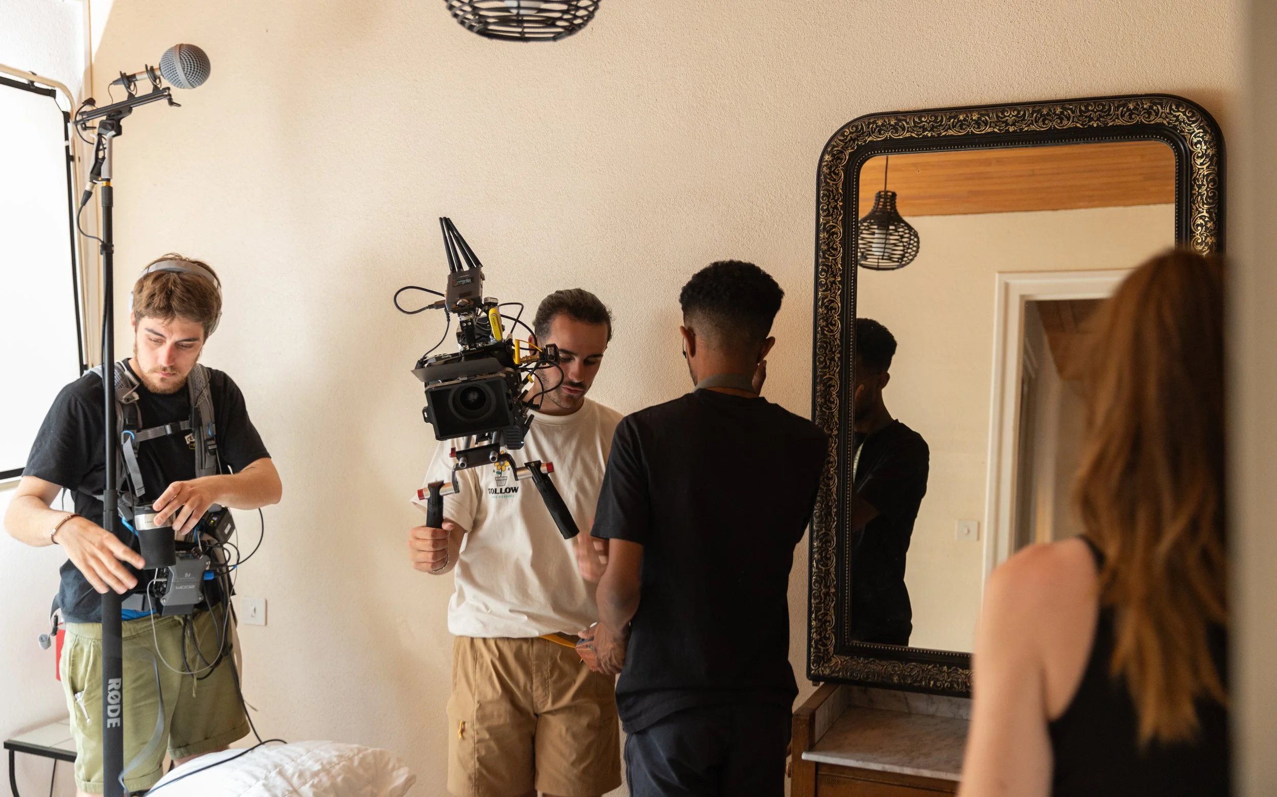 Équipe de tournage avec caméra et matériel dans une pièce, enregistrement vidéo d'une femme en noir vue de dos dans un décor intérieur