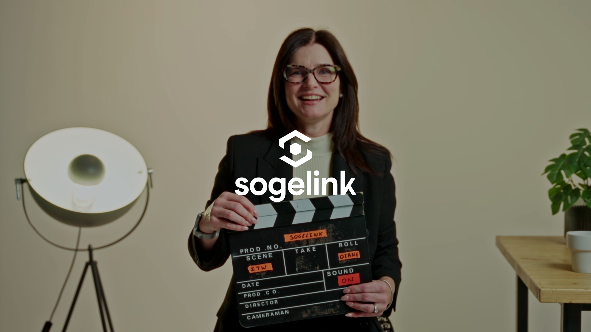 Miniature client : Sogelink (image d'une responsable de l'entreprise sogelink, elle tient un clap dans ses mains, elle s'apprête à donner une interview, avec logo blanc de l'entreprise sogelink)