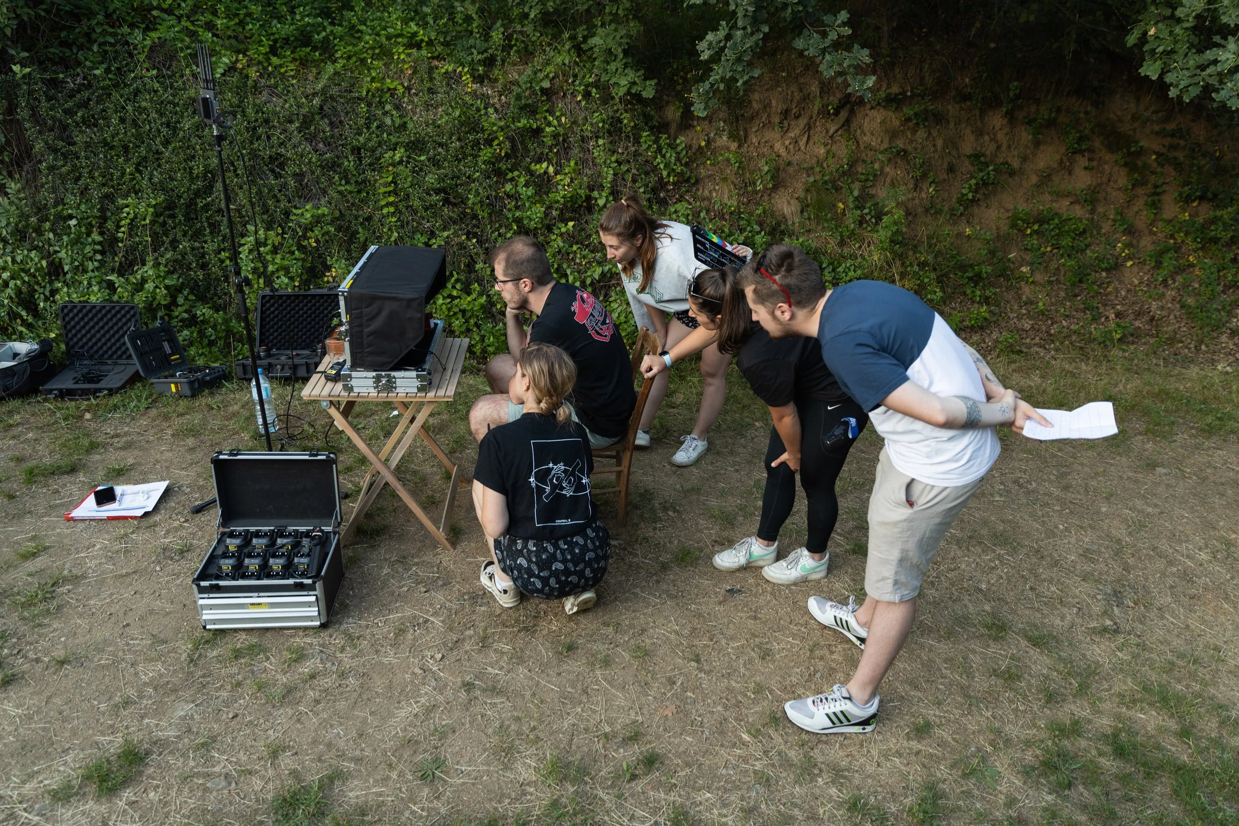 Groupe de personnes travaillant sur un projet de film ou vidéo en plein air, autour de matériel audiovisuel.