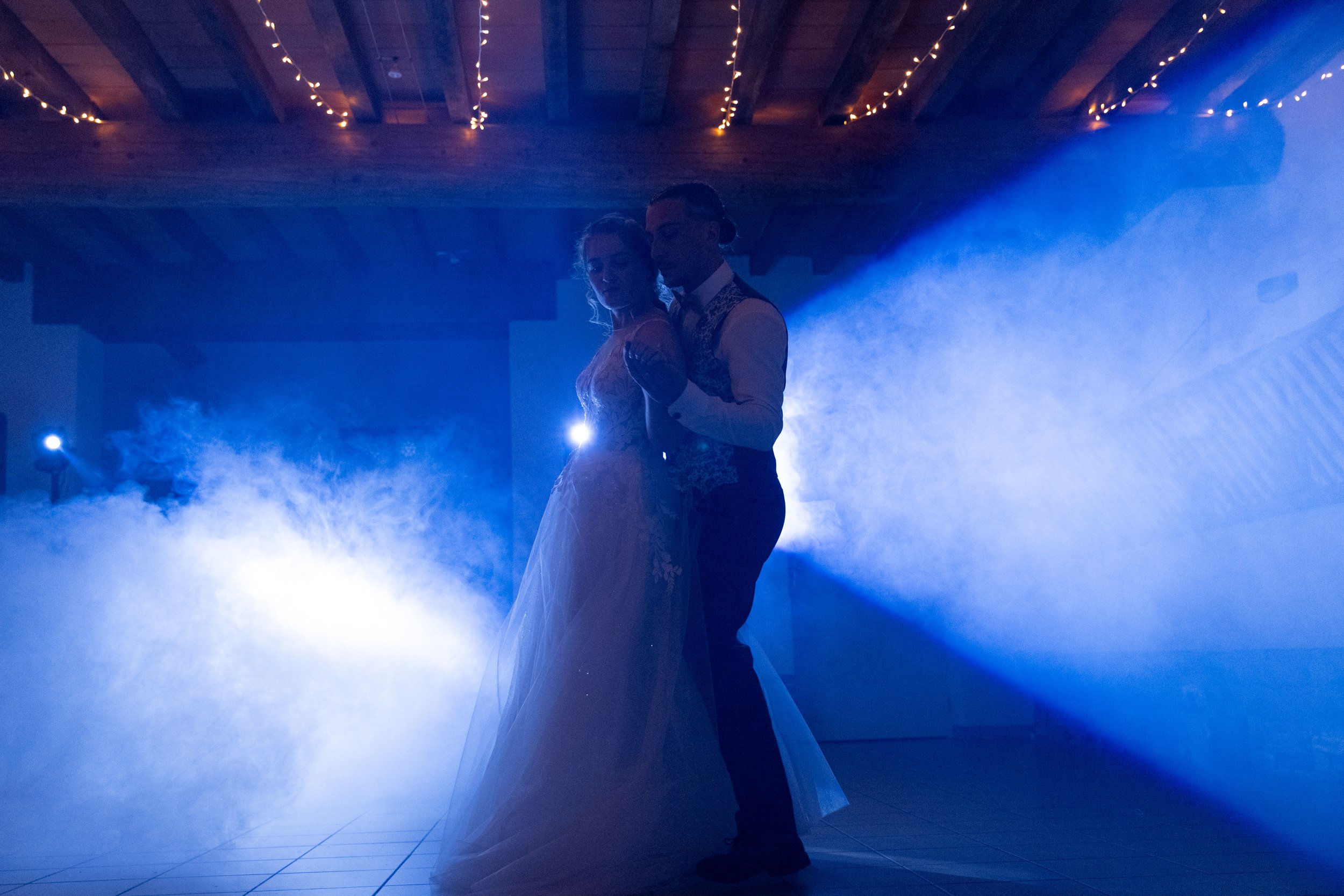 Un couple de mariés danse lors de leur mariage, éclairés par des lumières bleues et entourés de brume.