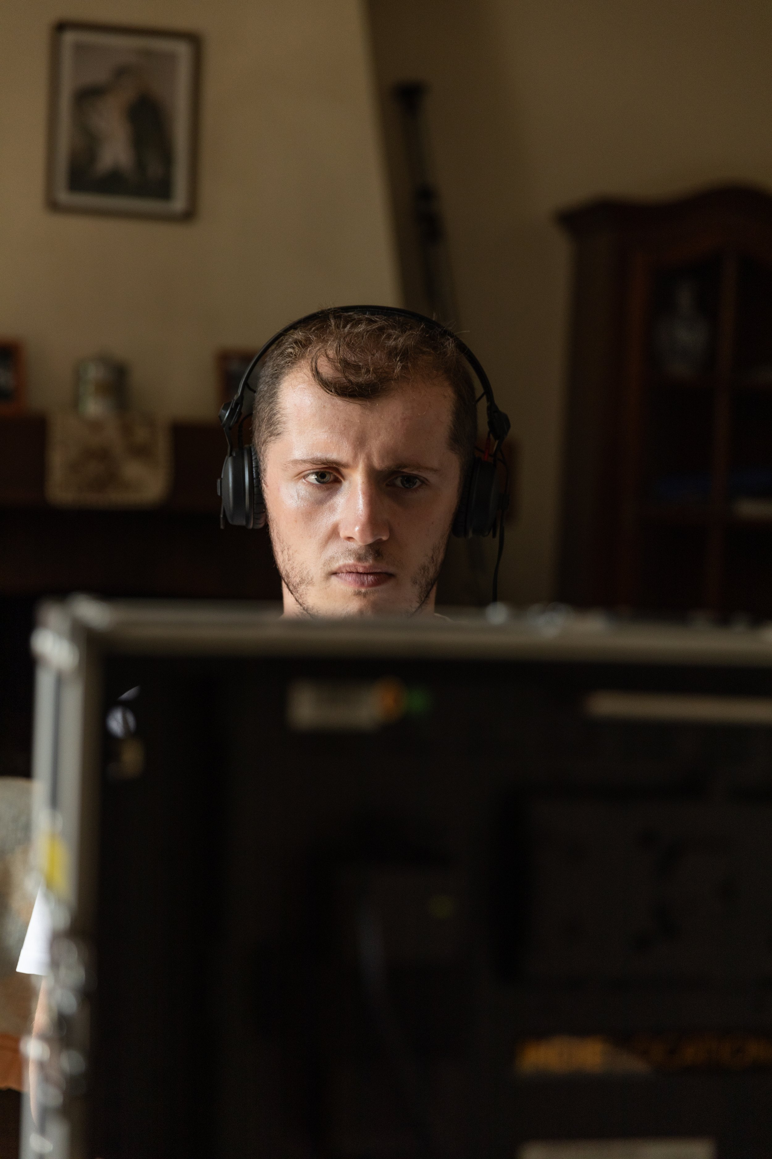 Jeune homme avec des écouteurs, concentré, regardant un écran d'ordinateur dans une pièce domestique.