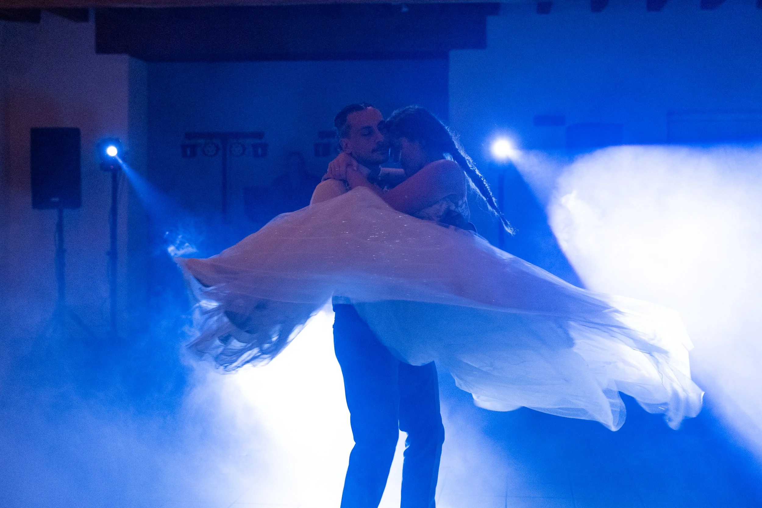 Un couple danse lors d'une soirée romantique avec des effets de lumière bleue et de fumée sur scène.