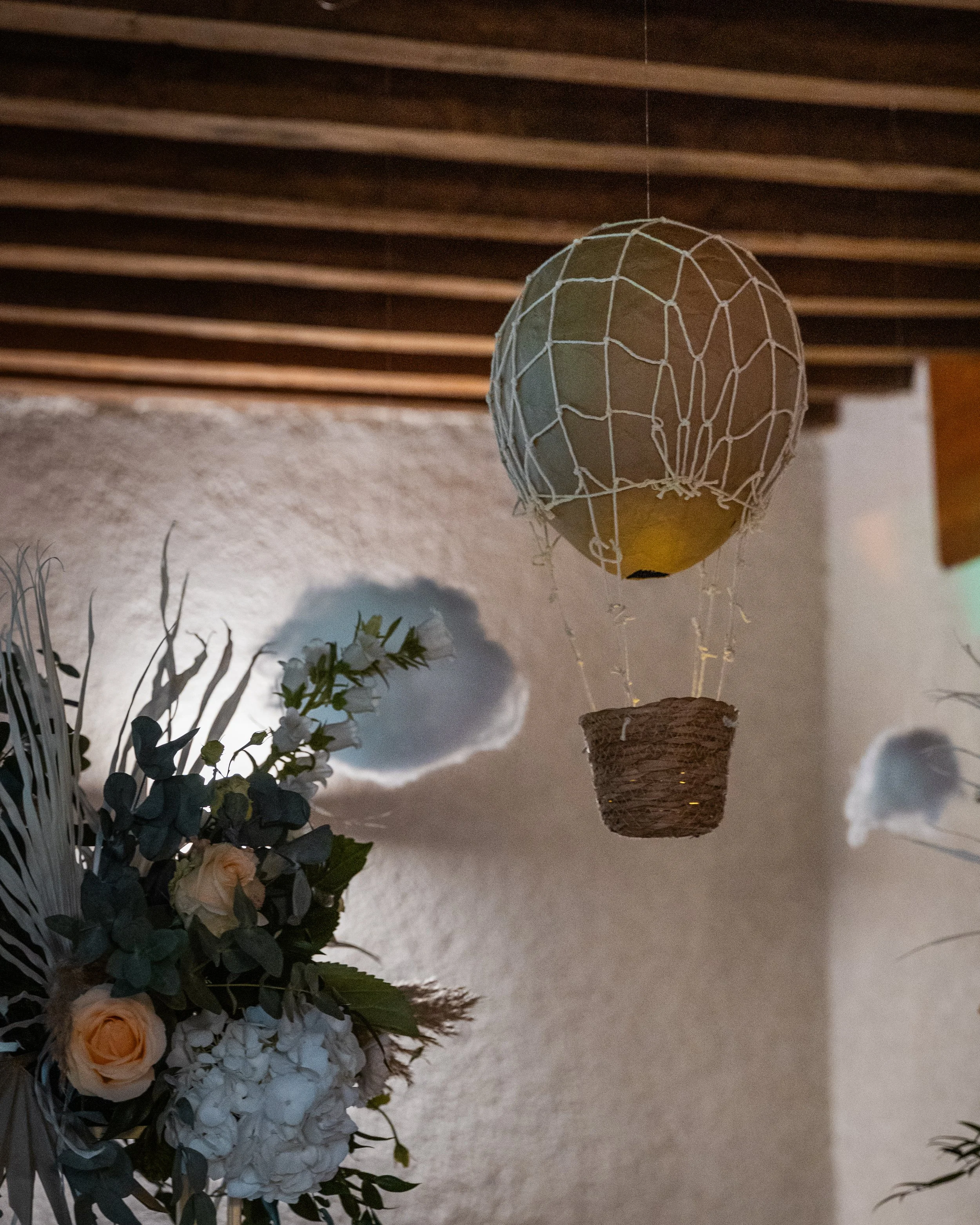 Un ballon de basketball est suspendu dans une cage en filet, avec un panier en dessous, décoré pour une occasion spéciale. À côté, il y a un arrangement floral avec des roses et des fleurs blanches, dans un décor intérieur avec un plafond en bois.