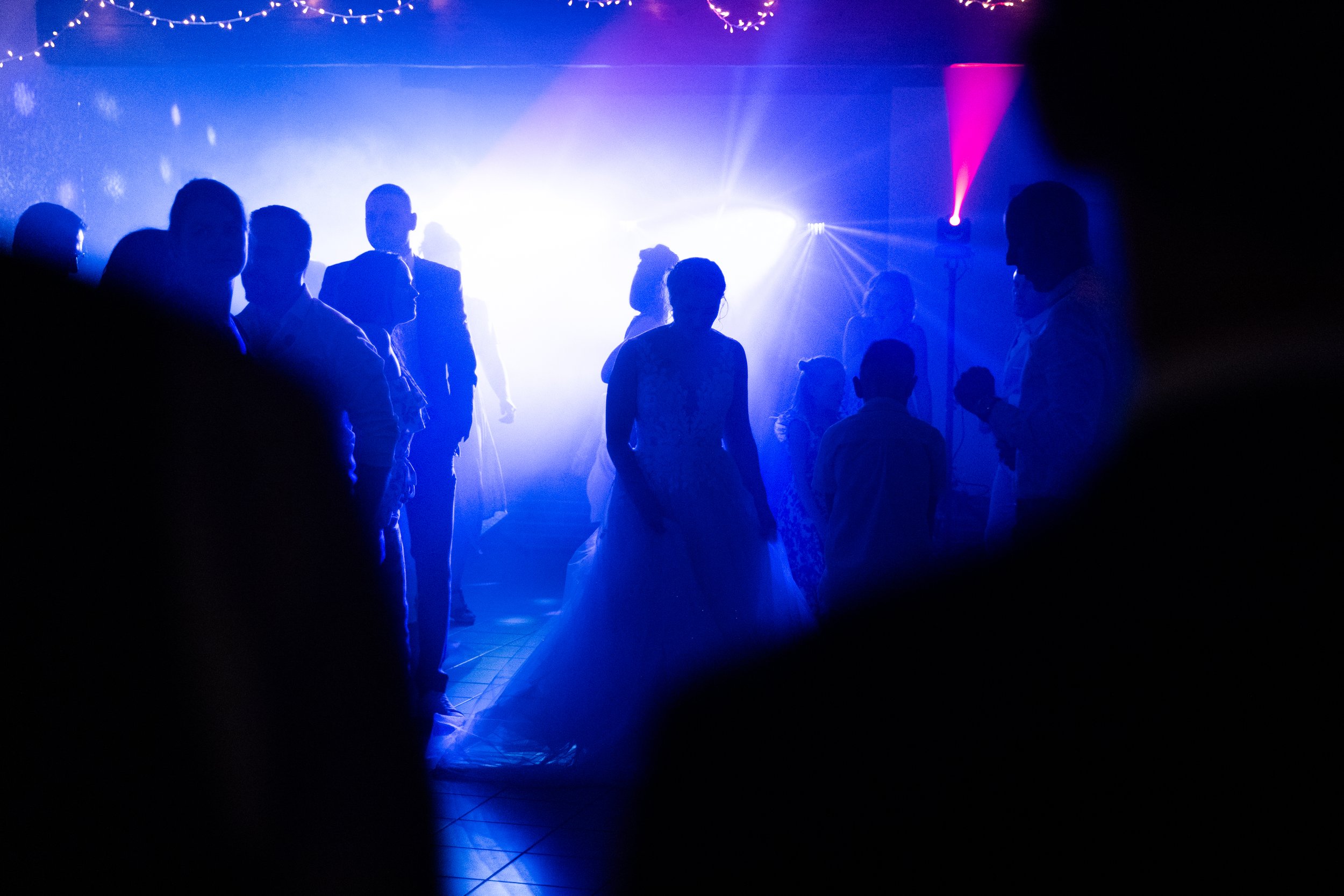 Silhouettes de personnes dansant dans une fête, éclairage violet et bleu, ambiance festive.