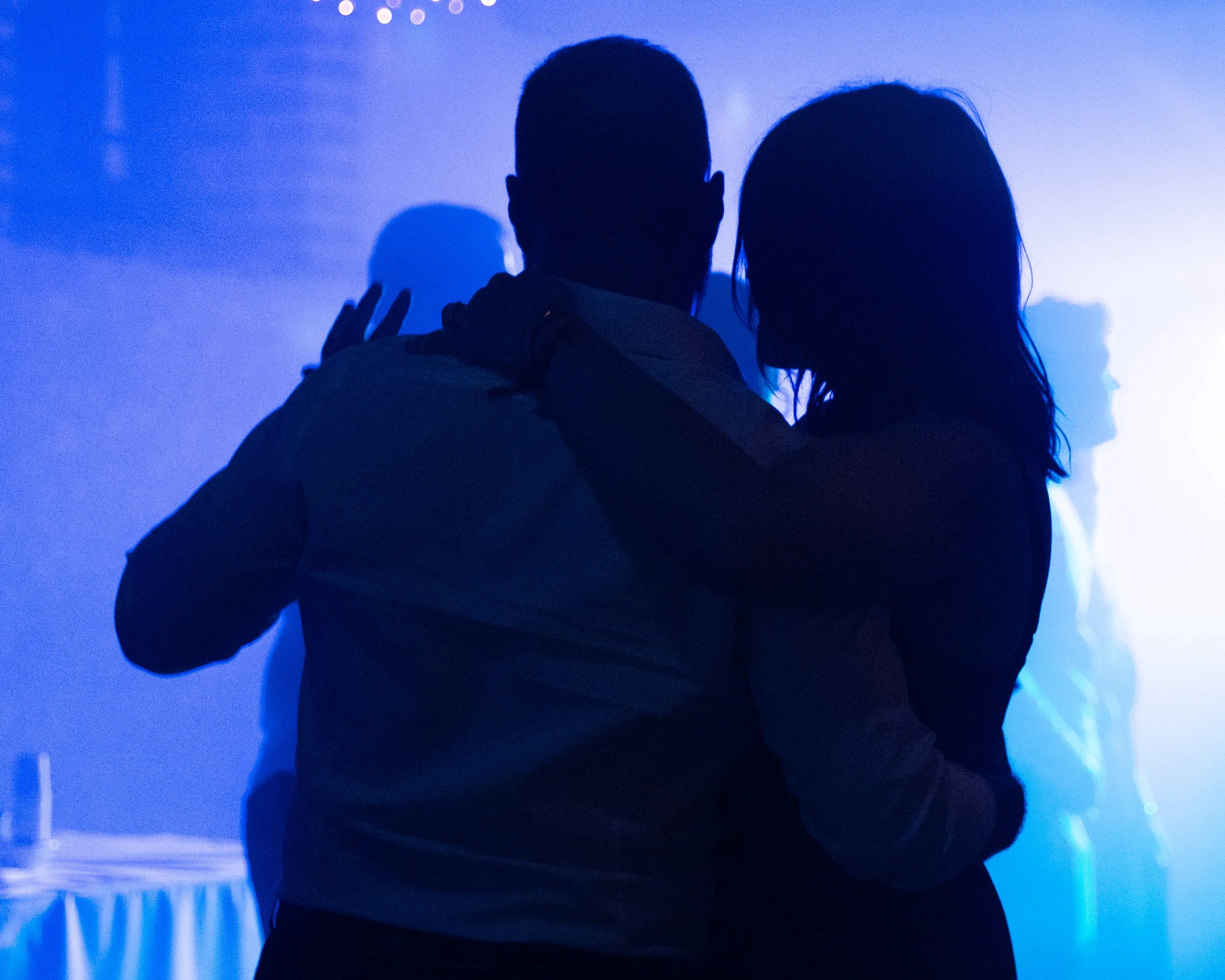 Silhouettes de deux personnes en train de danser dans une lumière bleue, avec d'autres personnes floues en arrière-plan.