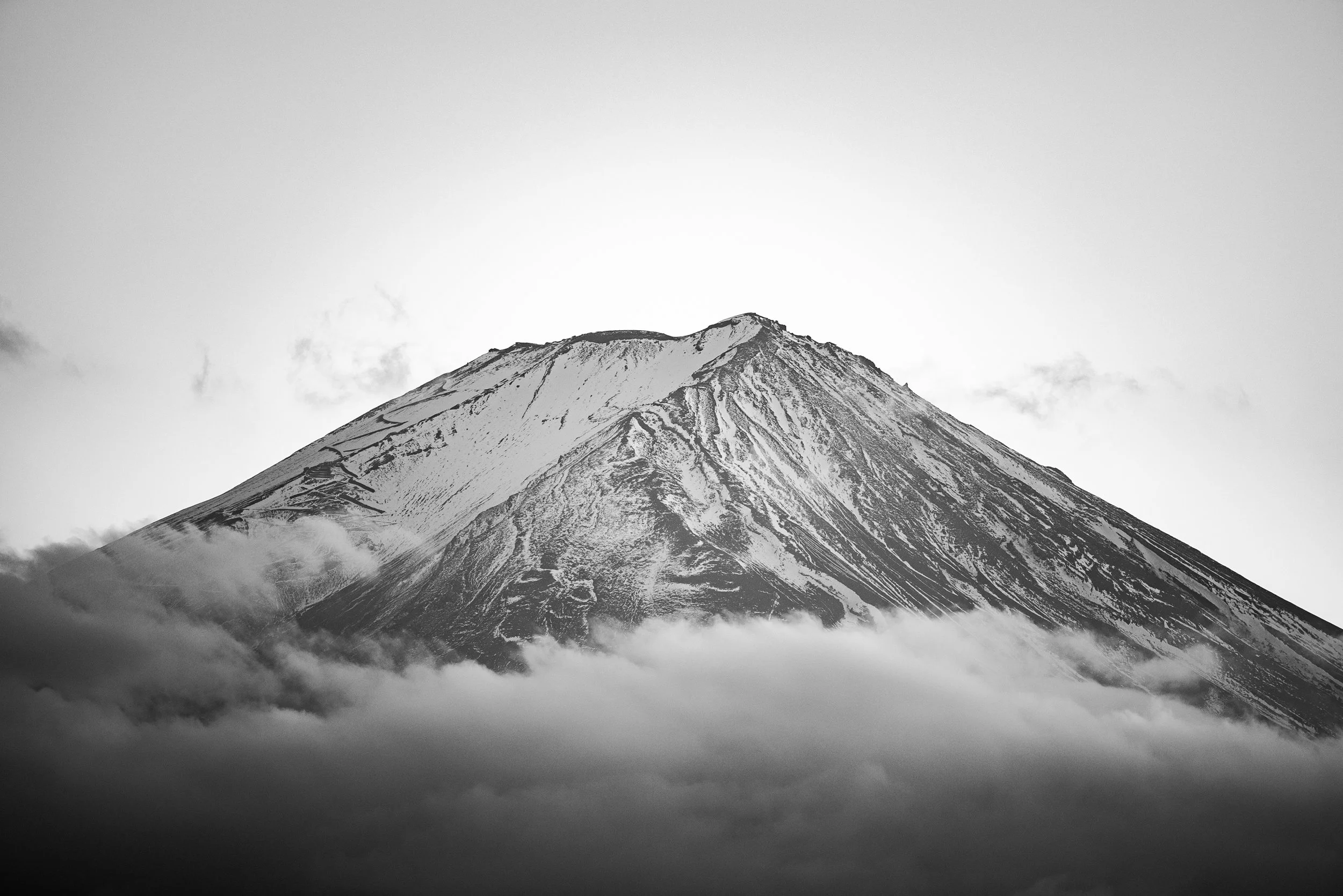 Montagne enneigée vue à travers des nuages, en noir et blanc.