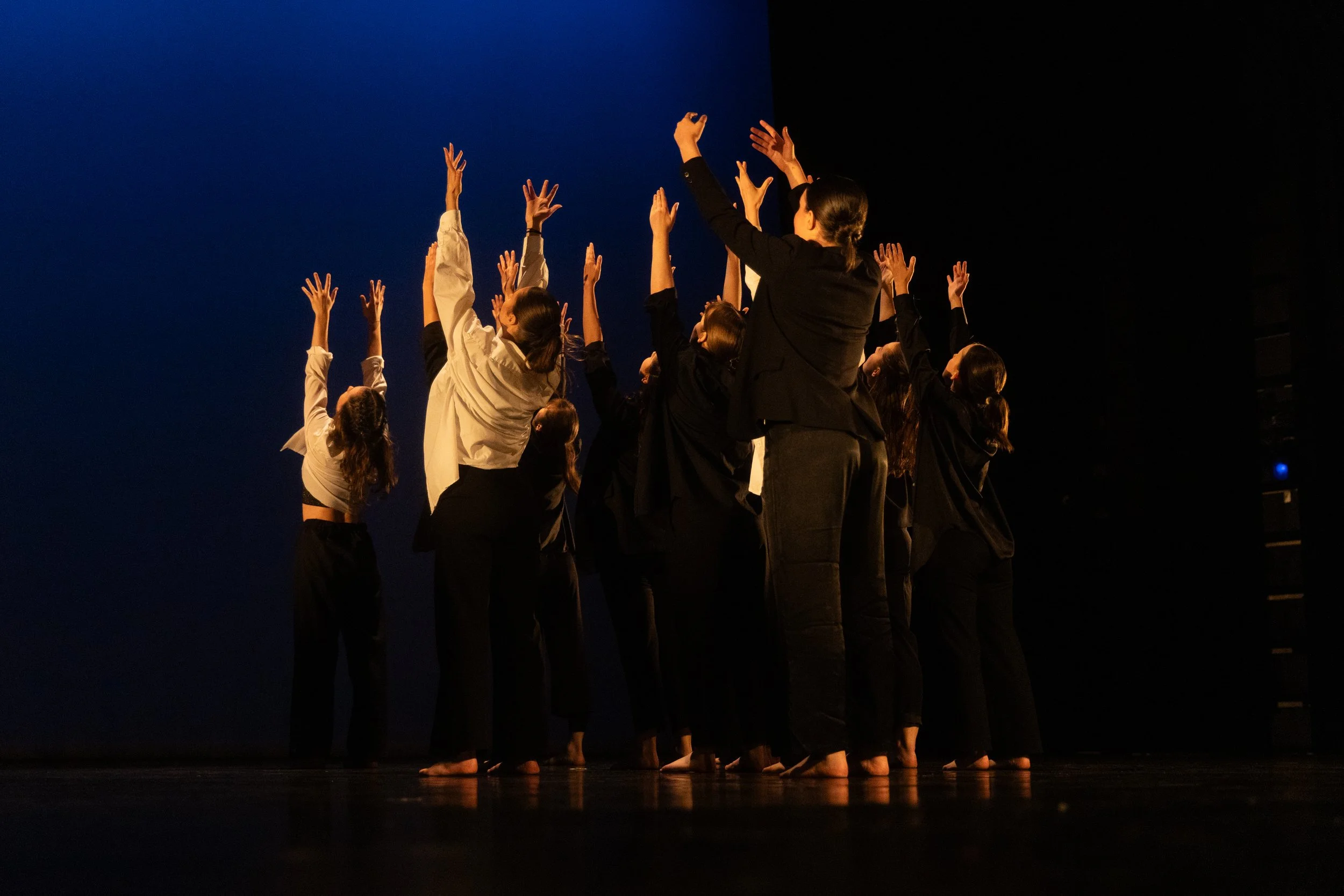 Des danseurs en costume noir et blanc en train de faire une performance sur scène avec un fond sombre et un éclairage chaud.