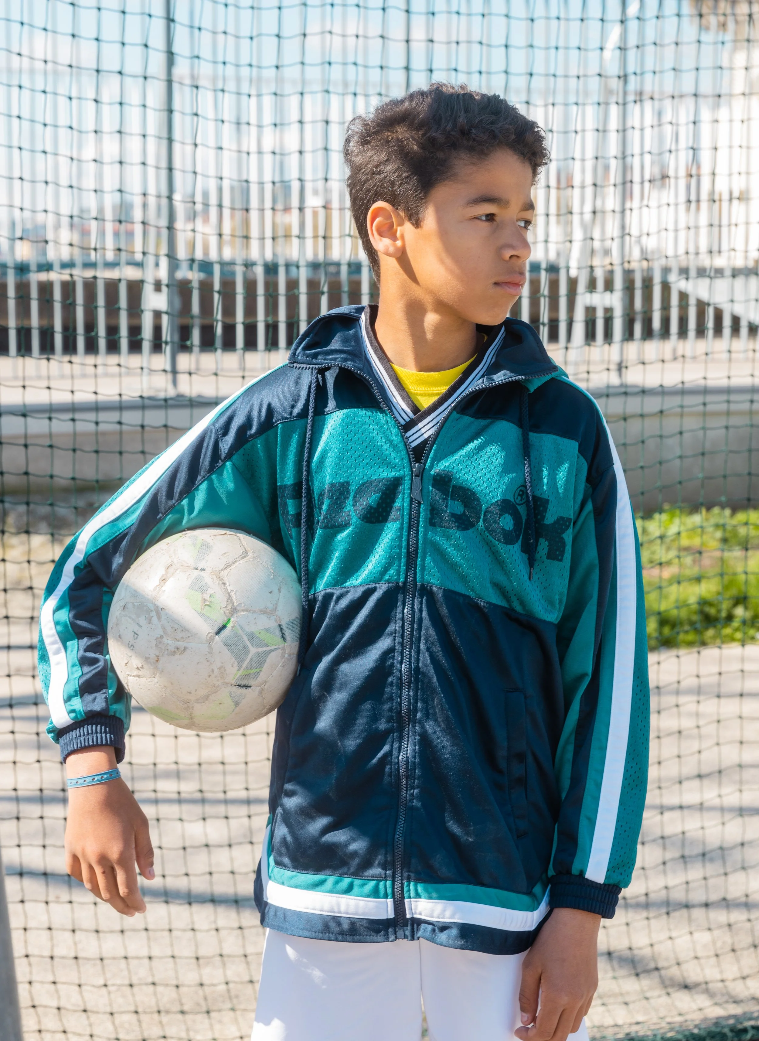Un jeune garçon avec un maillot de sport tiendra un ballon de football à la main sur un terrain de sport.