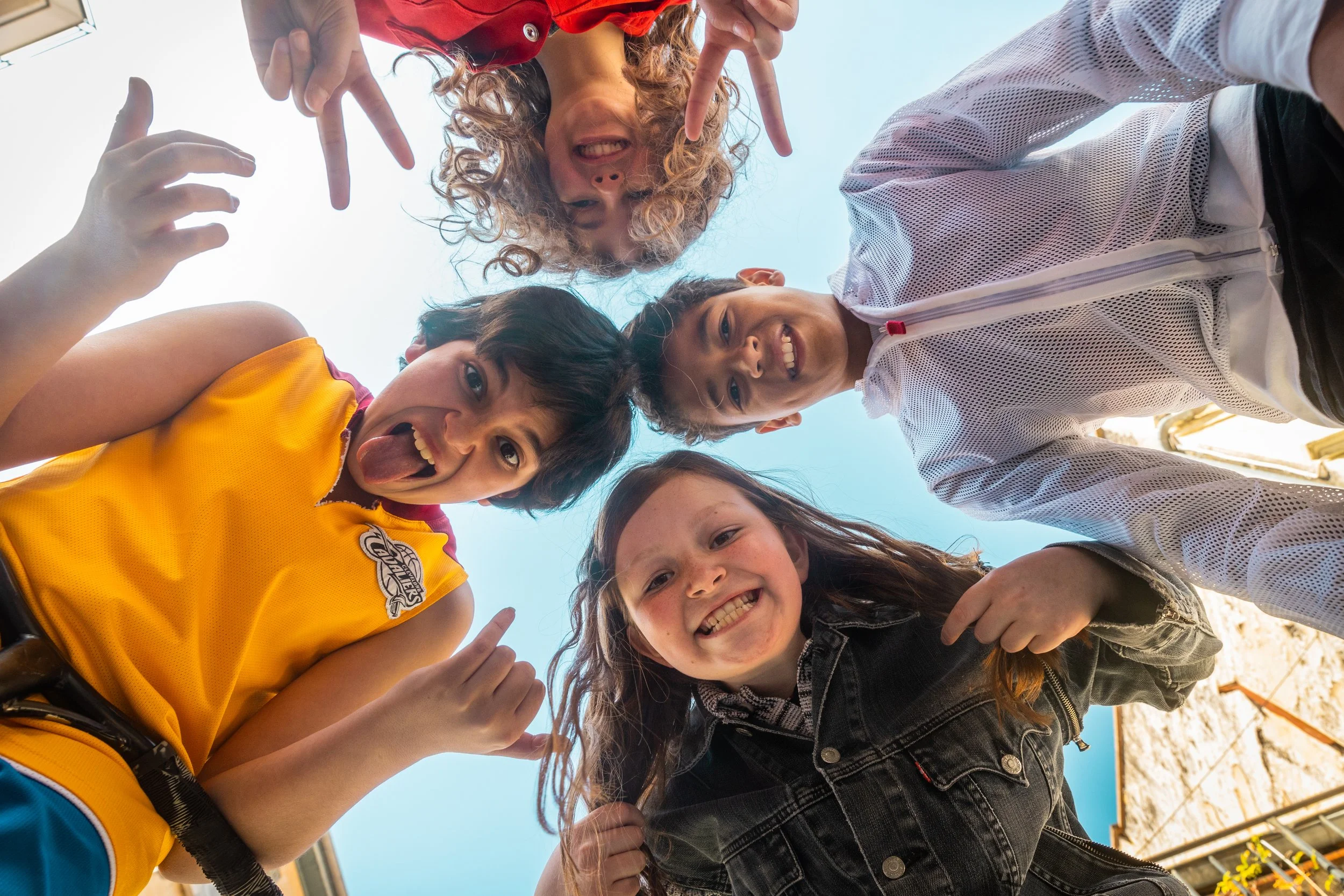 Groupe d'enfants souriants regardant vers la caméra, vu du dessous, avec le ciel en arrière-plan.