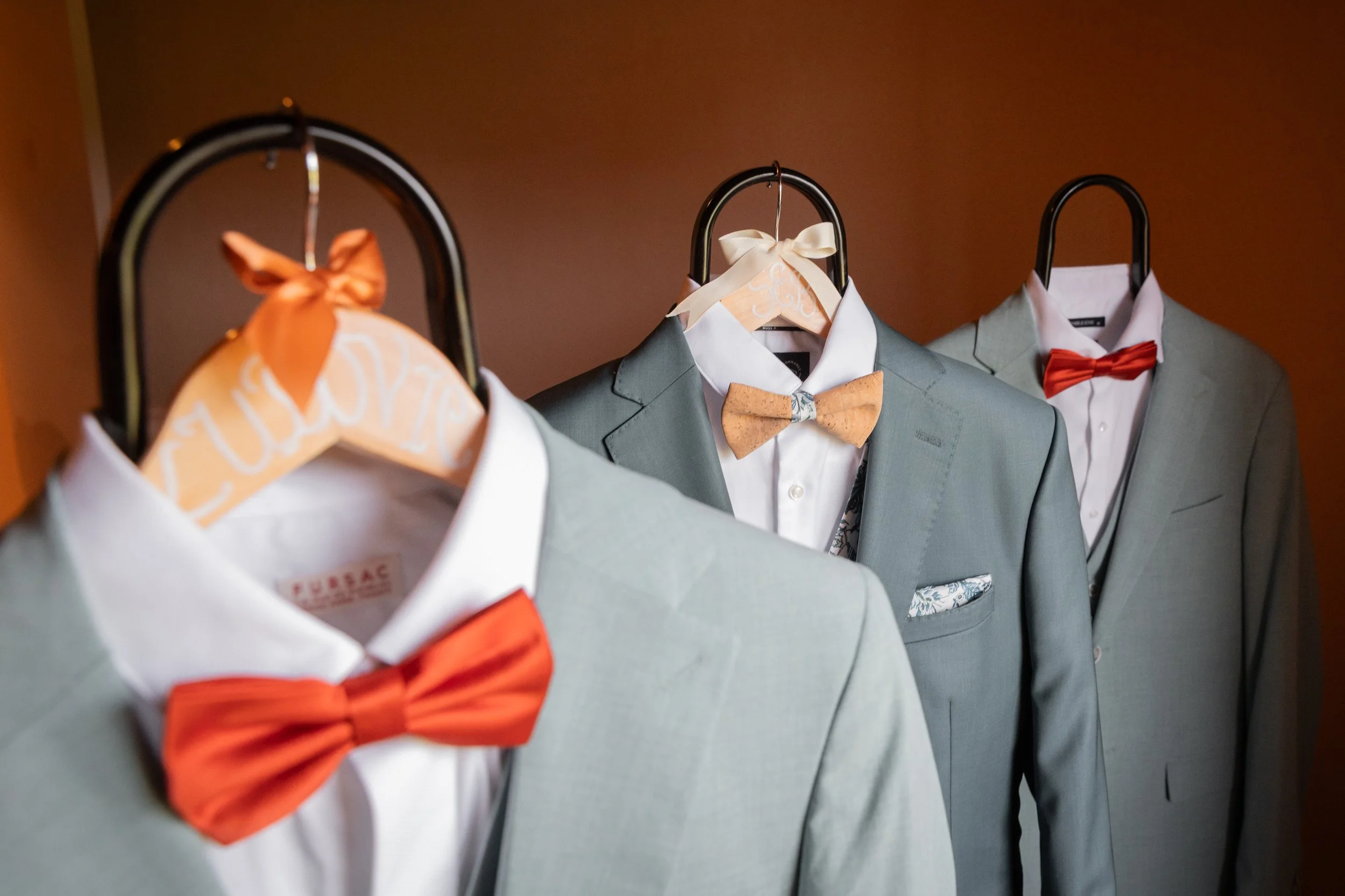 Costumes de marié dans des vestes gris clair avec différentes couleurs de nœuds papillons, suspendus sur des cintres