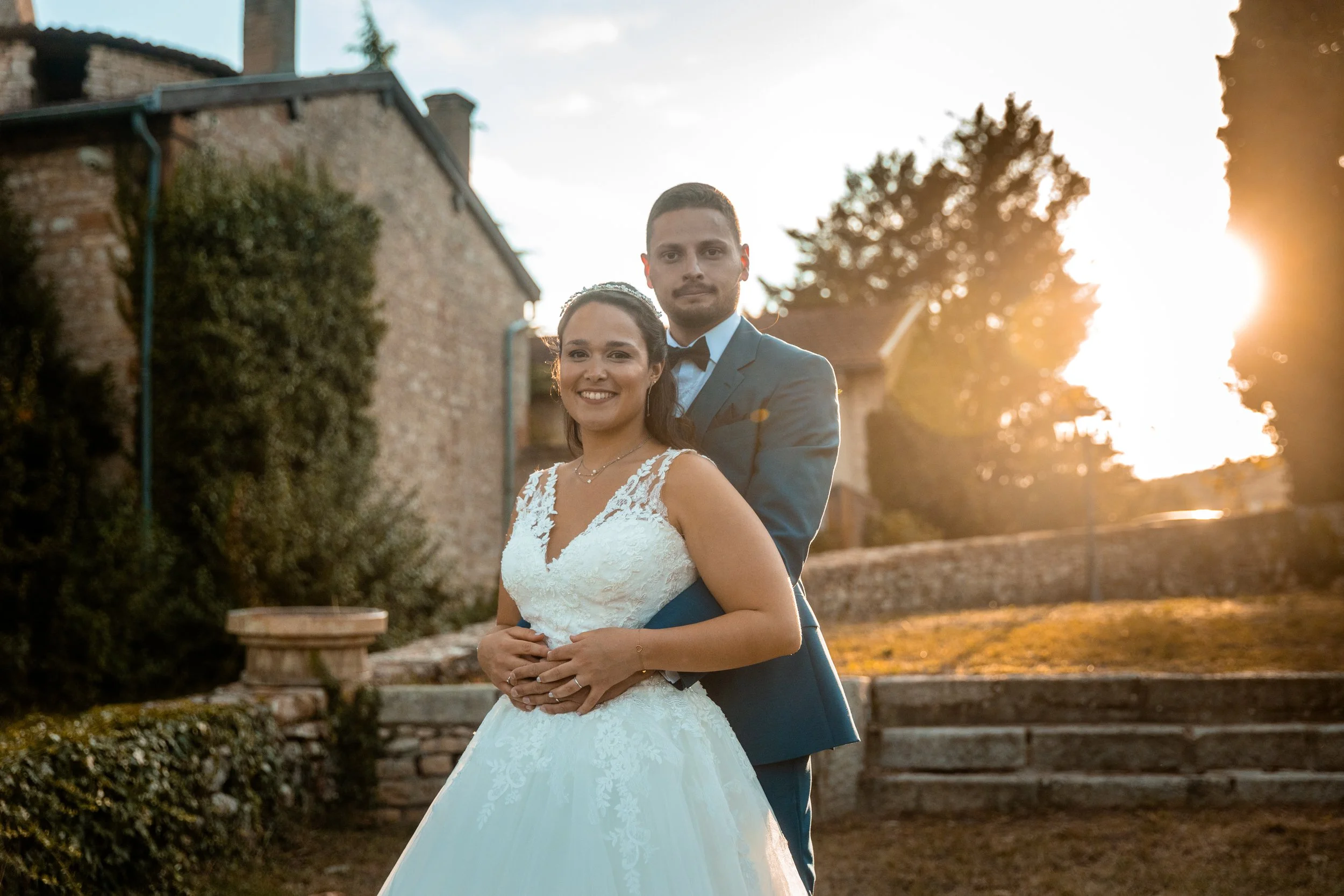 Un couple en robe de mariée et costume de mariage posant ensemble à l'extérieur au coucher du soleil.
