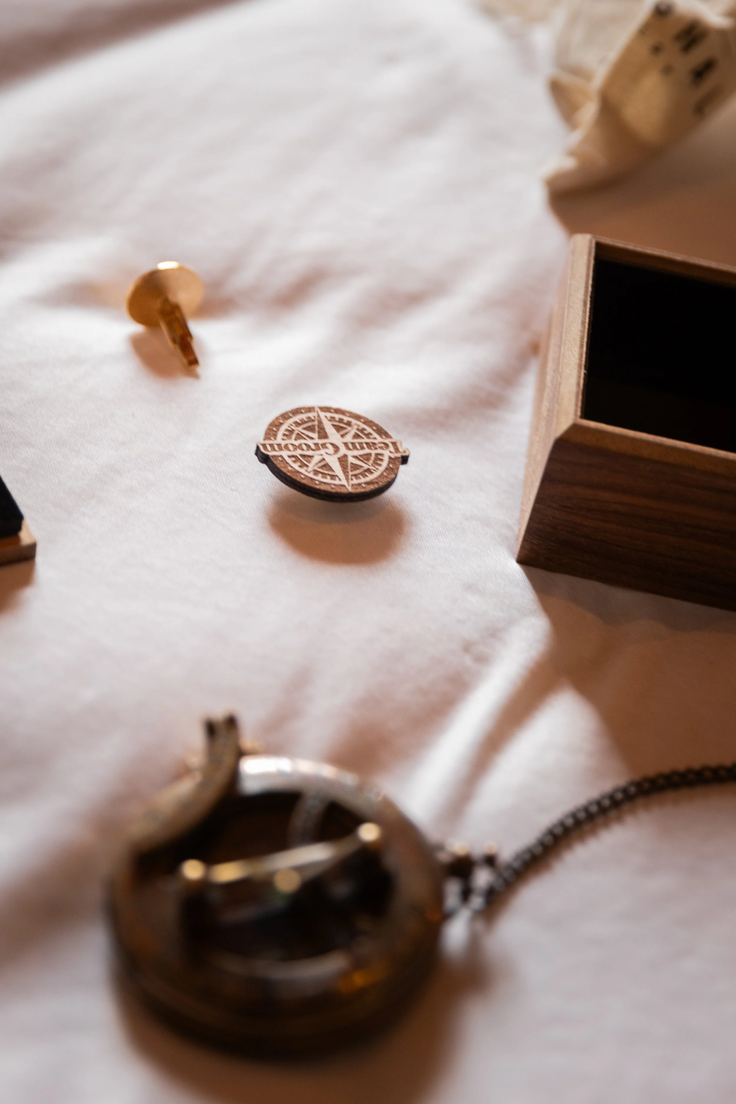 Objets en bois et métal dispersés sur une surface en tissu blanc, incluant une pièce de monnaie, une clé, et une boîte en bois ouverte.