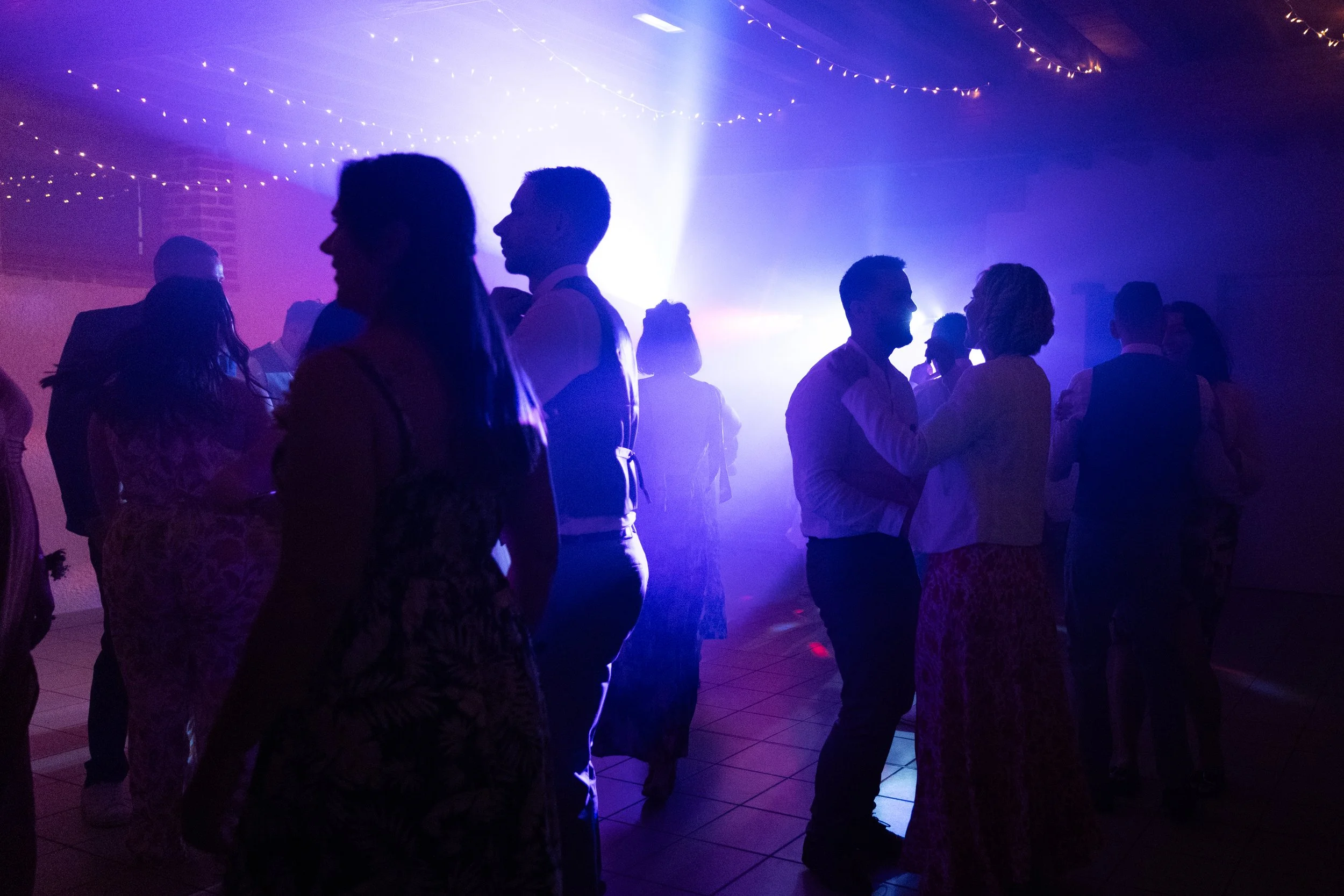 Des personnes dansent lors d'une soirée avec des lumières violettes et des guirlandes lumineuses au plafond.