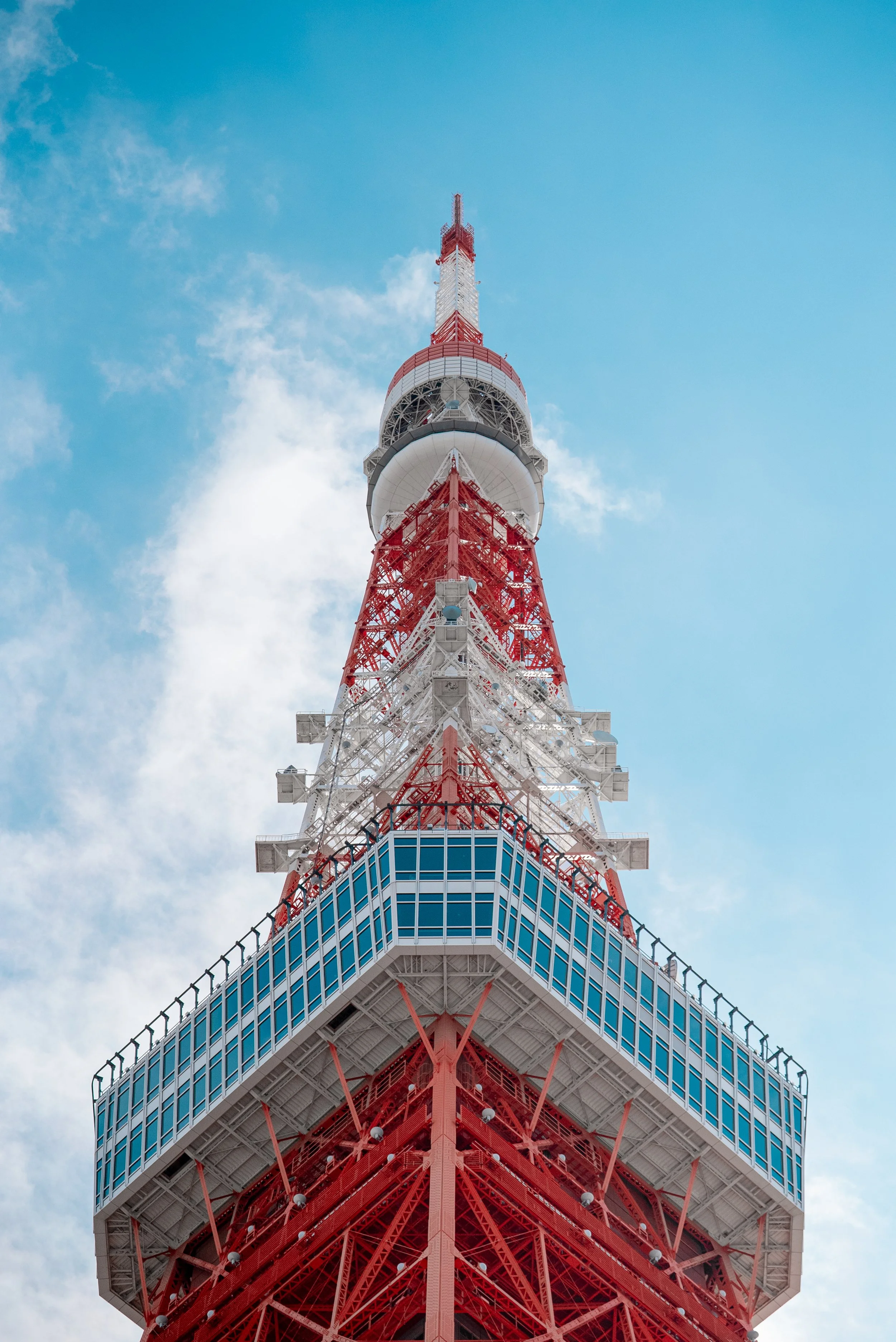 Vue de bas de la tour de Tokyo avec une structure en acier rouge et blanc, contre un ciel bleu avec quelques nuages.