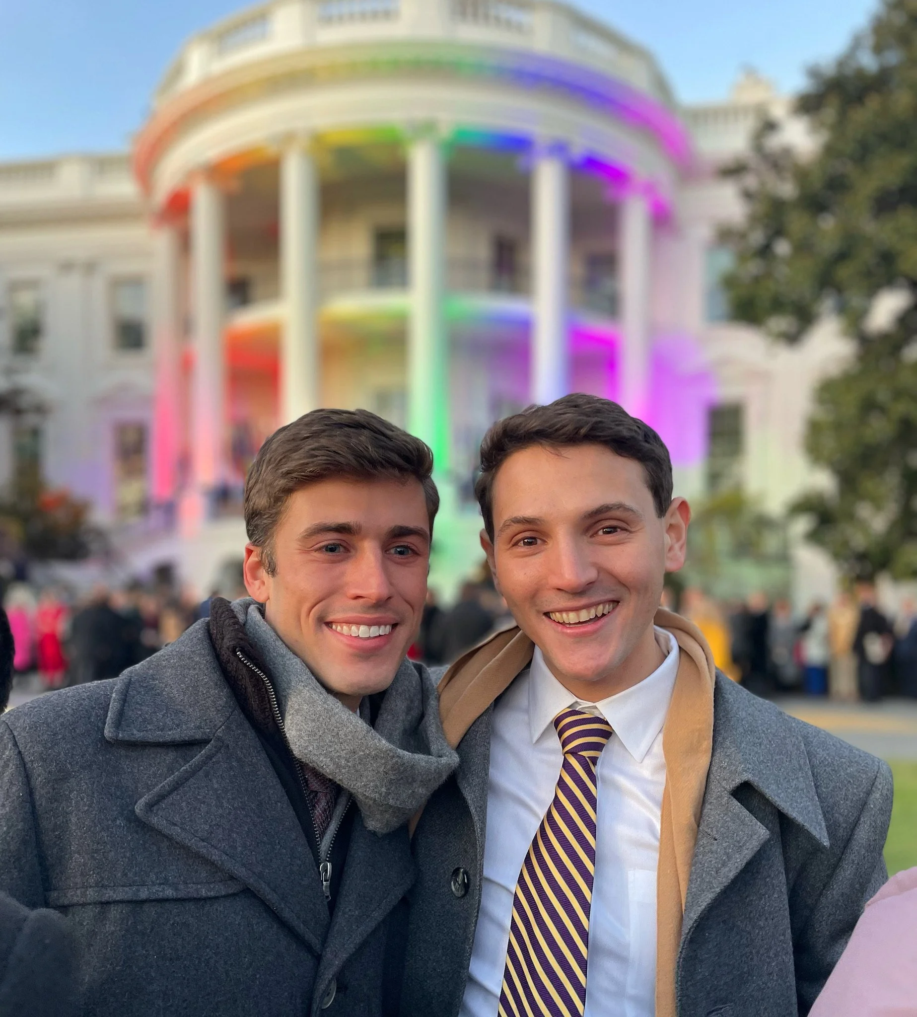 Daniel and his husband stand in front of the white house lit in pride colors
