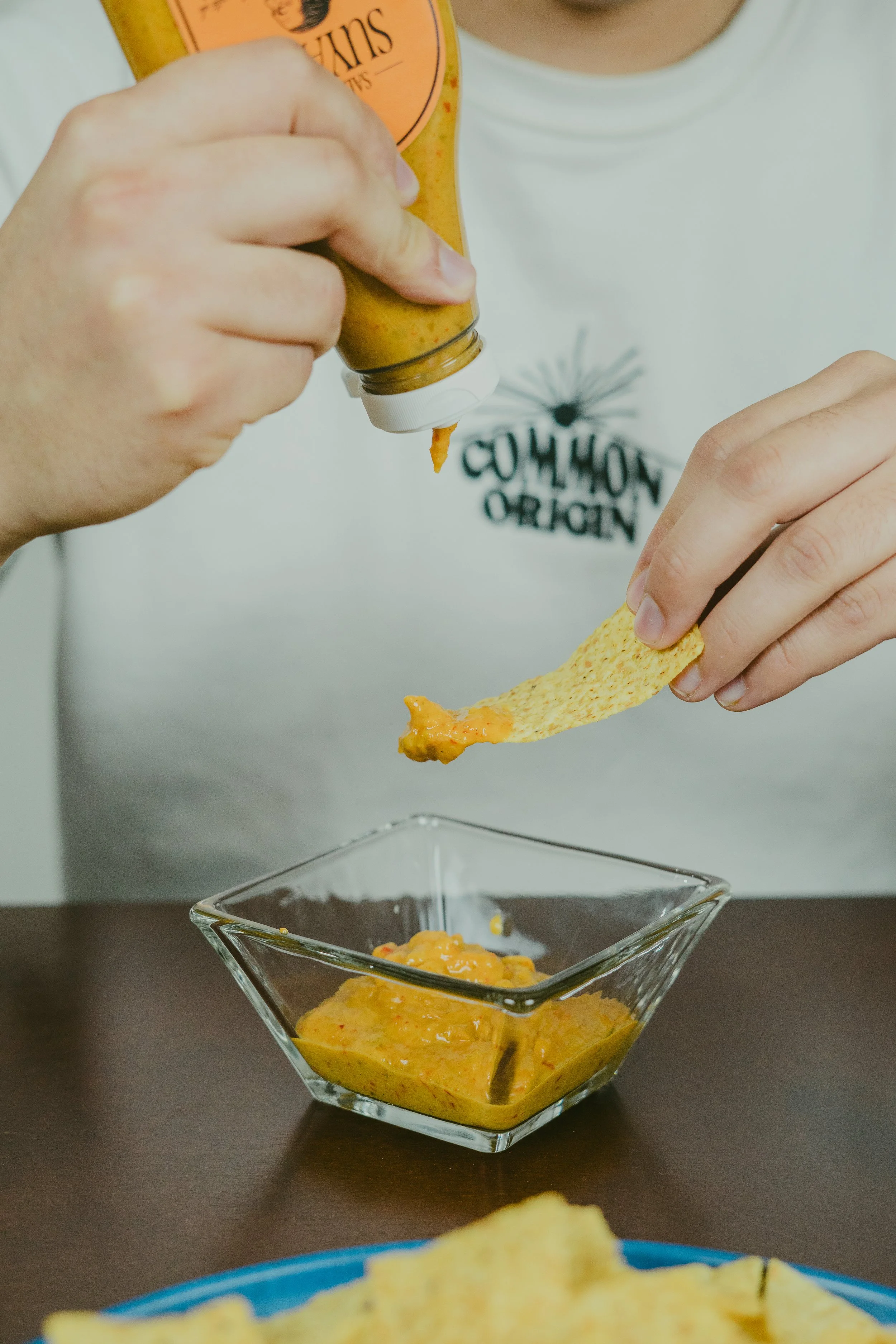 Persona untando salsa picante en una tortilla con totopos en un plato azul.