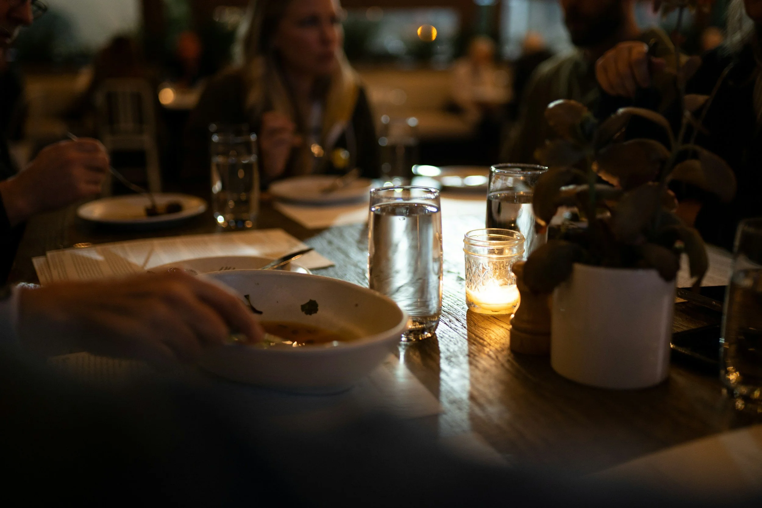 People sitting at a dimly lit dinner table with glasses of water, plates, and a candle