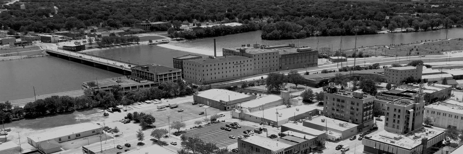 Black and white aerial view of an urban industrial area with buildings, parking lots, and a river running through the city.