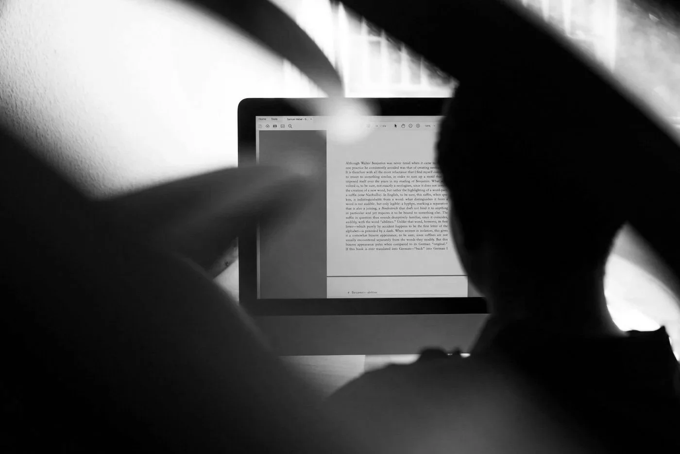 Silhouette of a person working on a computer with a document open on the screen, in black and white.