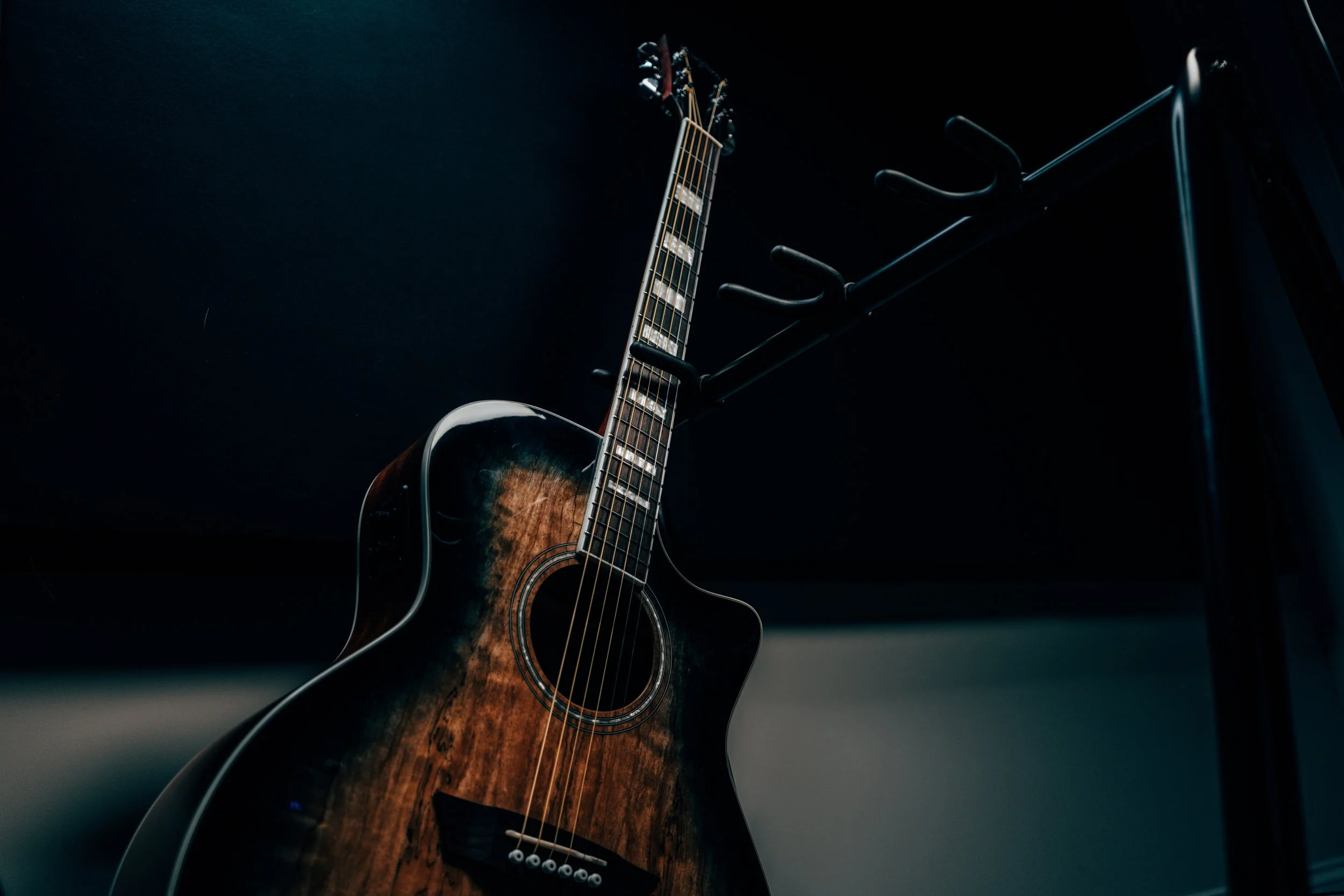 An acoustic guitar hanging on a black hook rack against a dark background.
