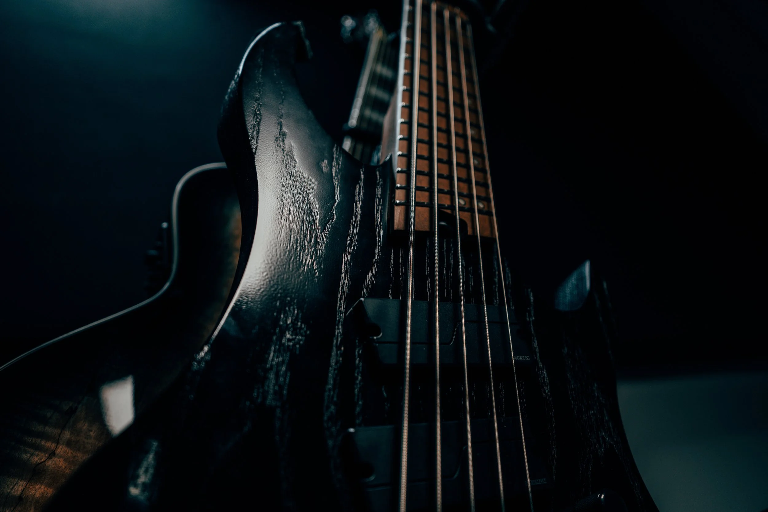 Close-up of a dark electric bass guitar with a glossy black body and strings, illuminated in a low-light setting.